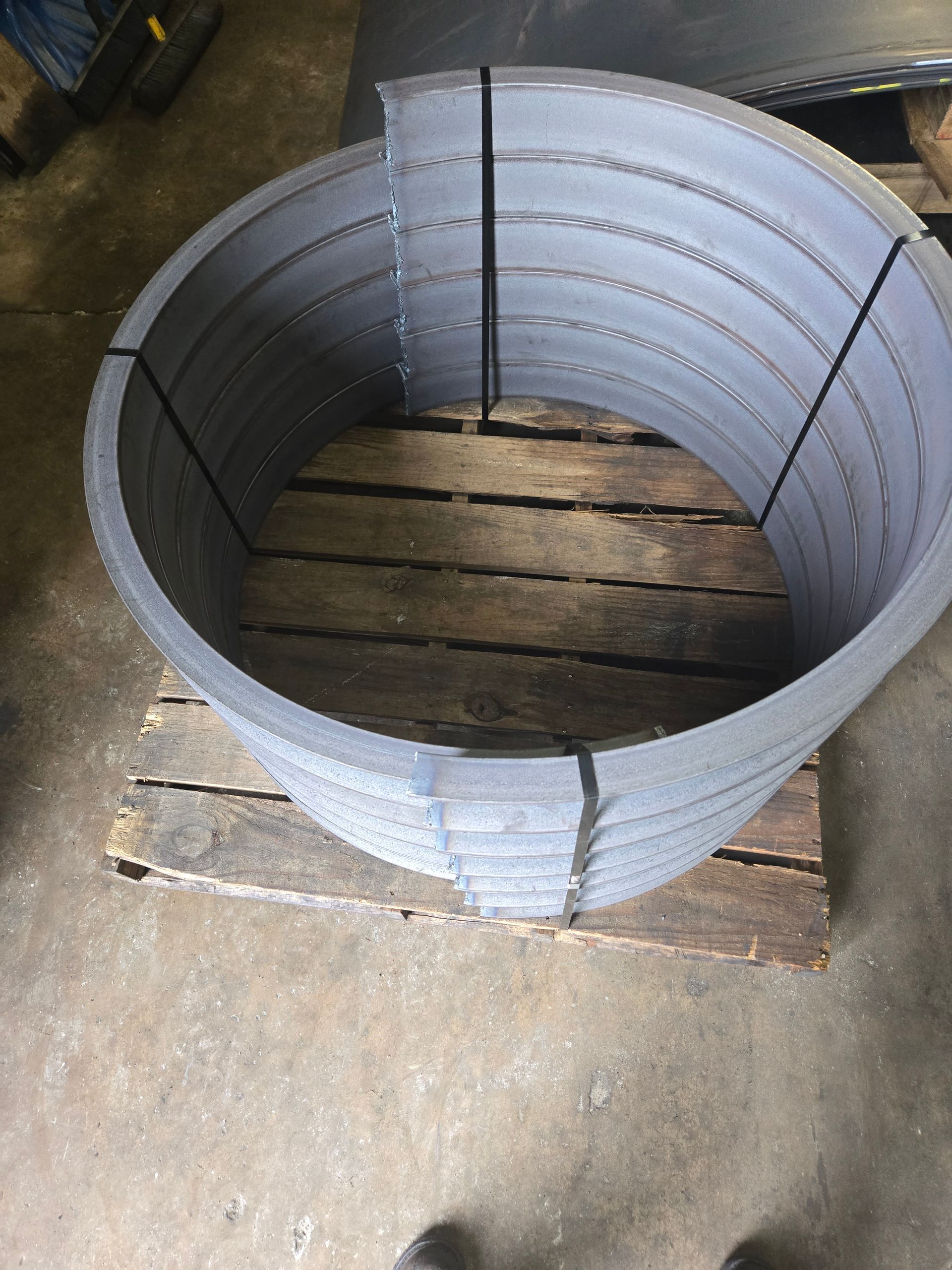 Metal rings stacked on a wooden pallet, held together by black straps.