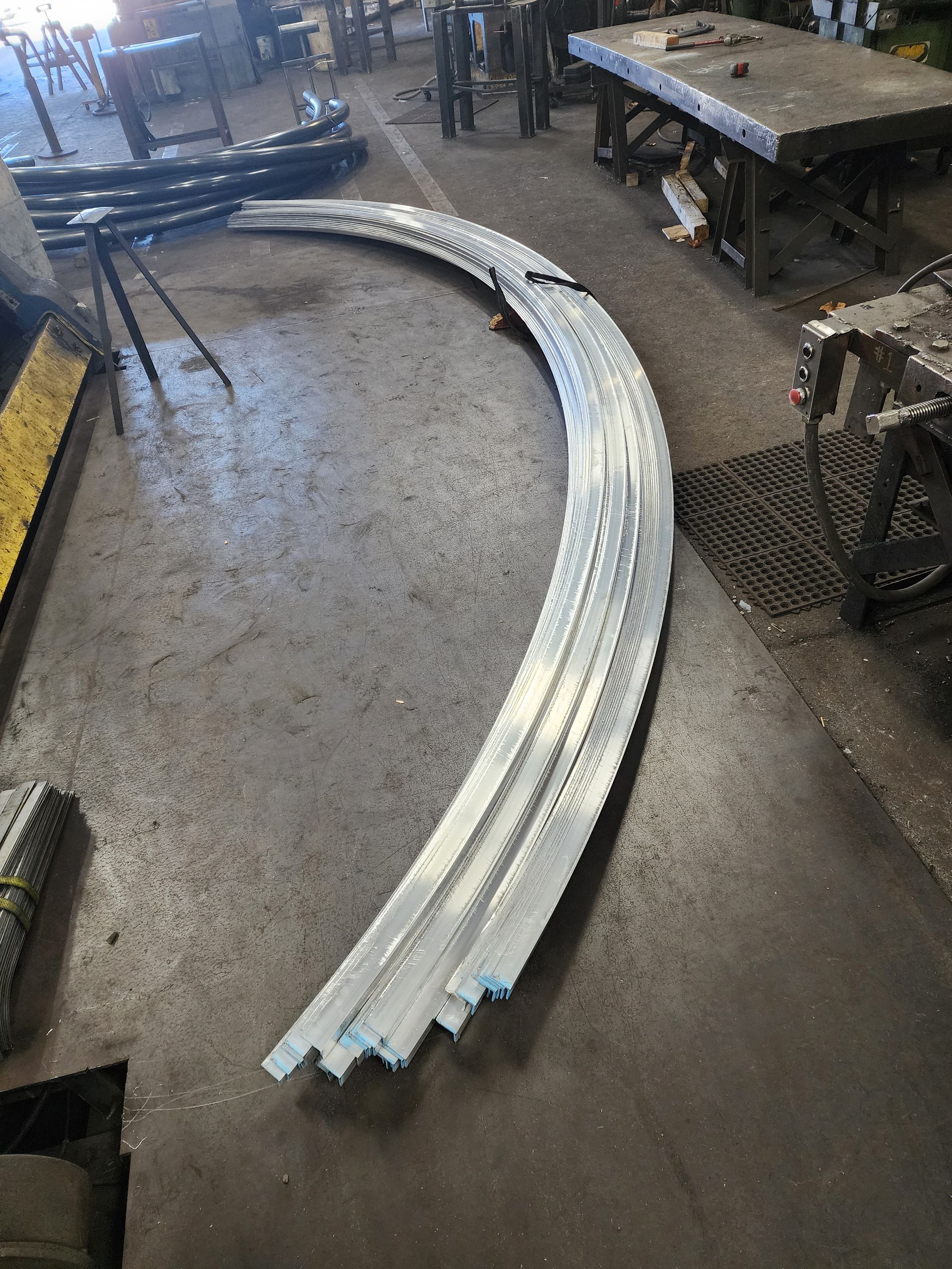 Curved metal strips stacked on a shop floor.