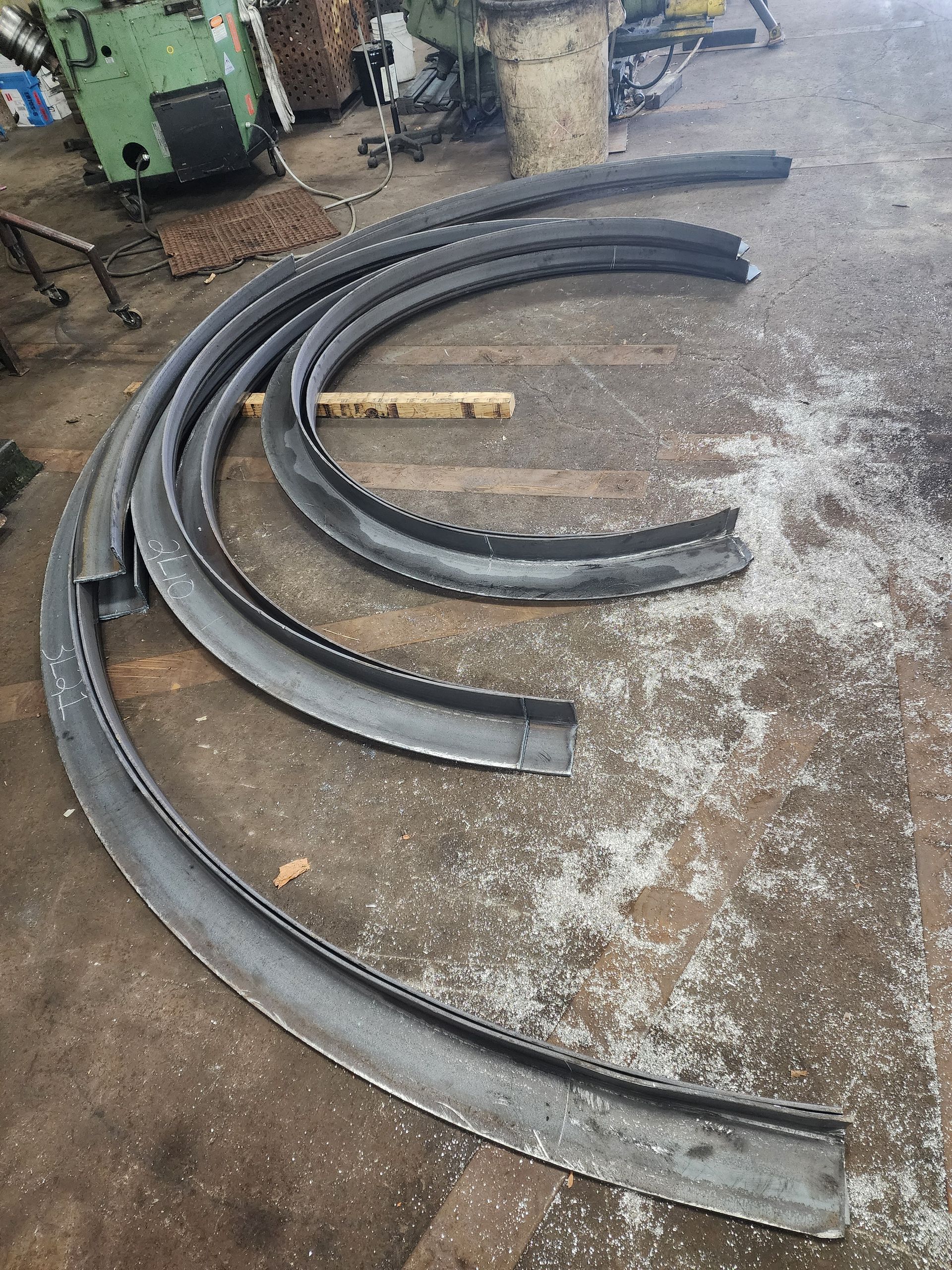 Curved metal beams on a workshop floor, possibly for construction, surrounded by metal shavings.