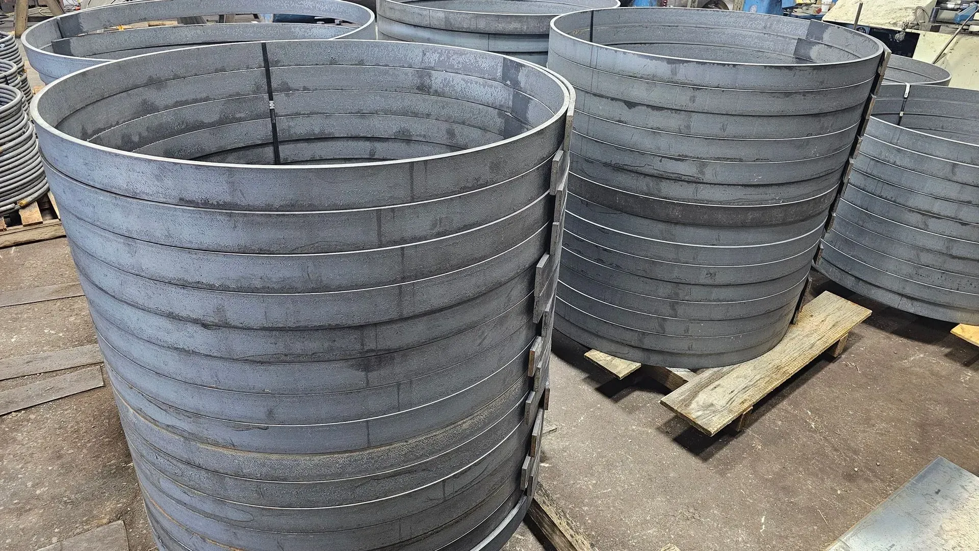 Metal cylinders stacked on a wooden pallet, with horizontal cutouts throughout the structures.