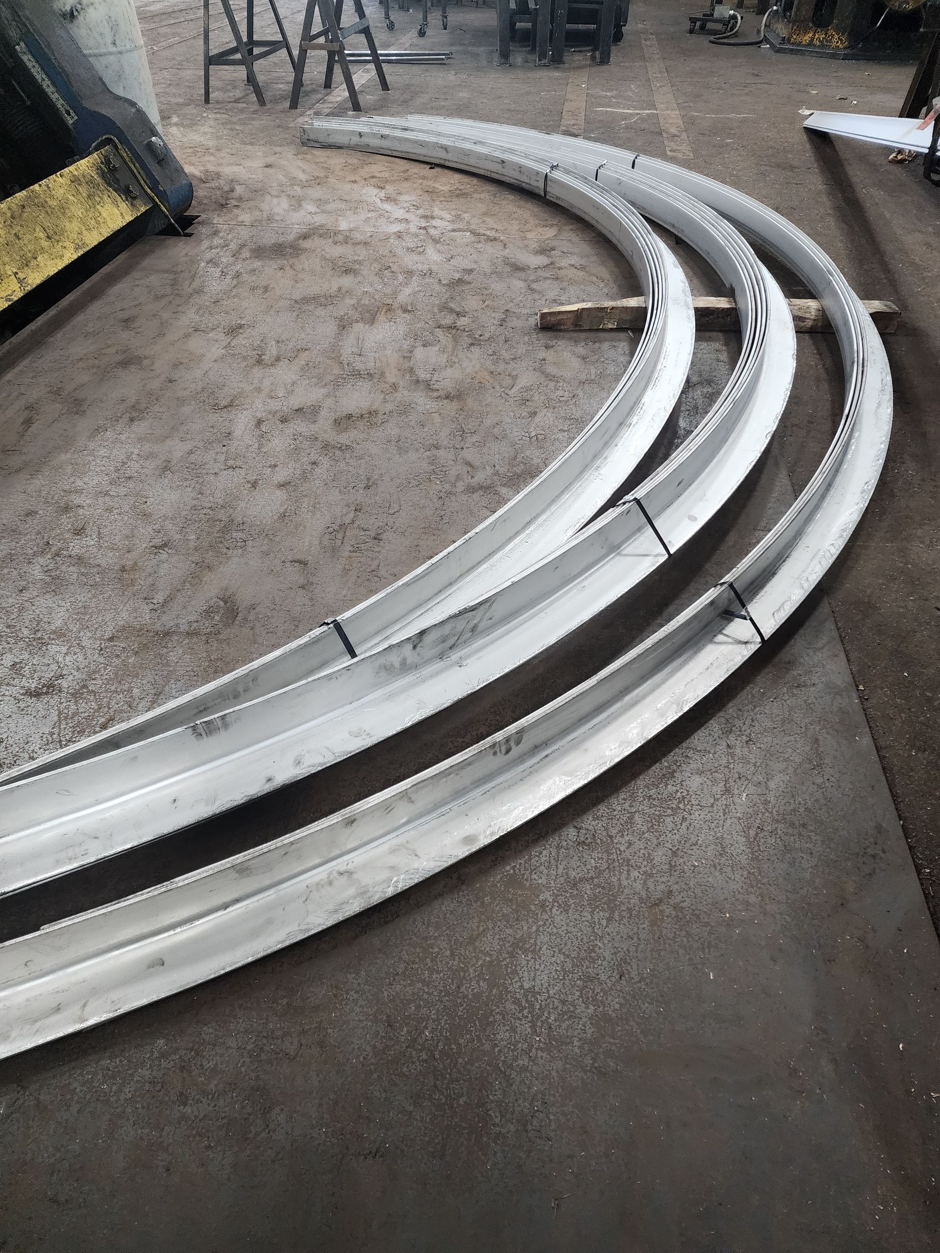 Curved metal beams, freshly cut, stacked on a workshop floor.