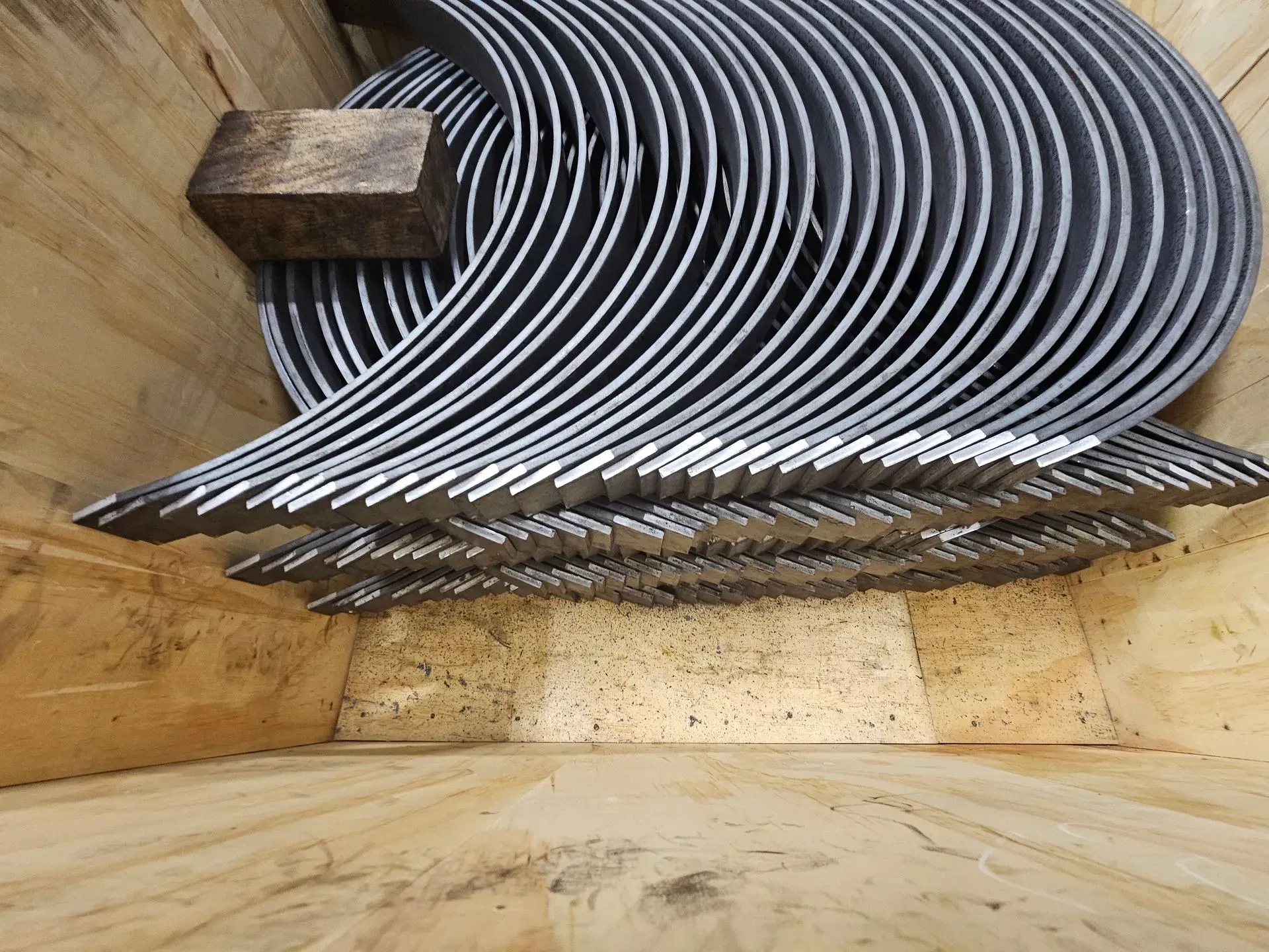 Metal, crescent-shaped components stacked inside a wooden crate.