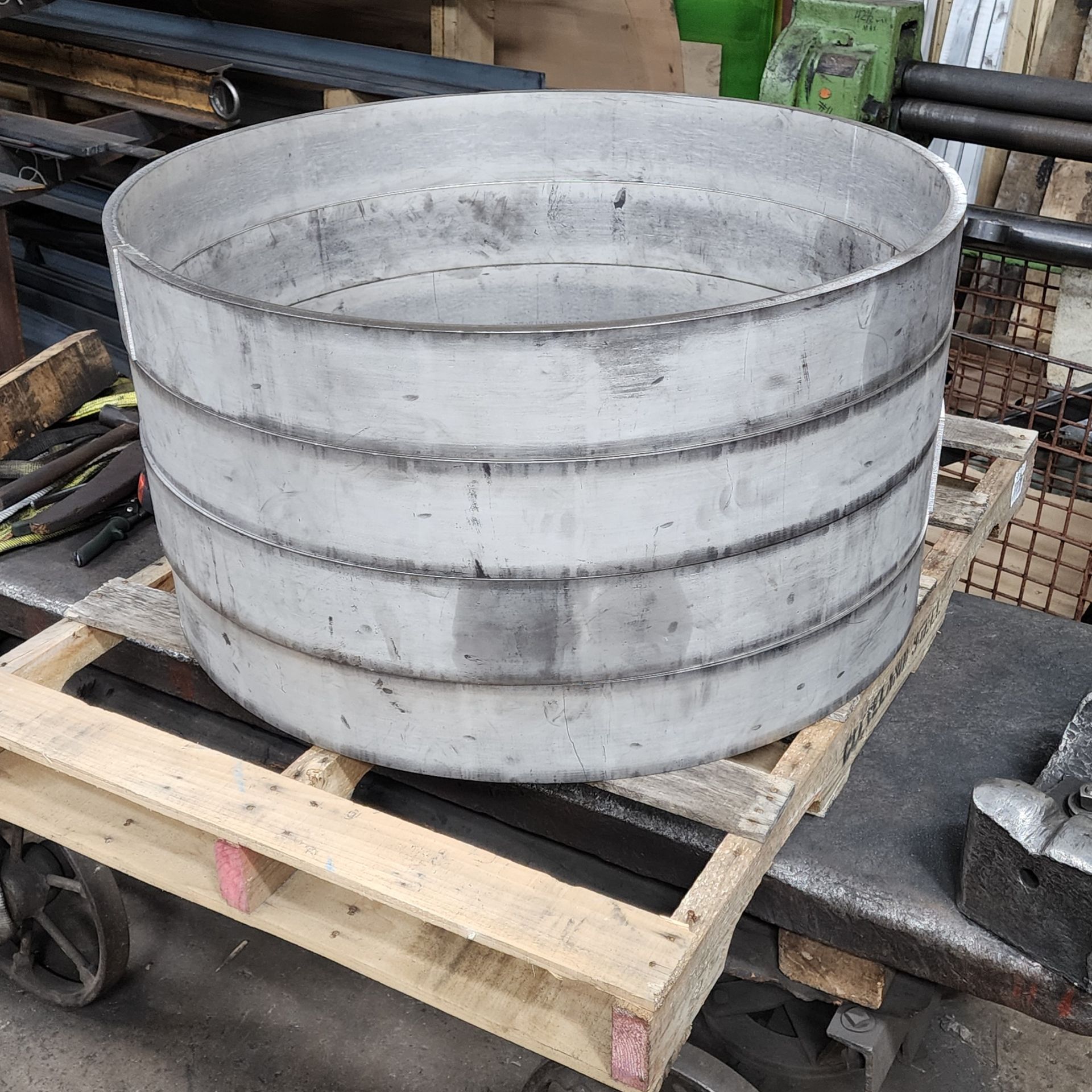Large stainless steel cylindrical metal container resting on a wooden pallet in a workshop.