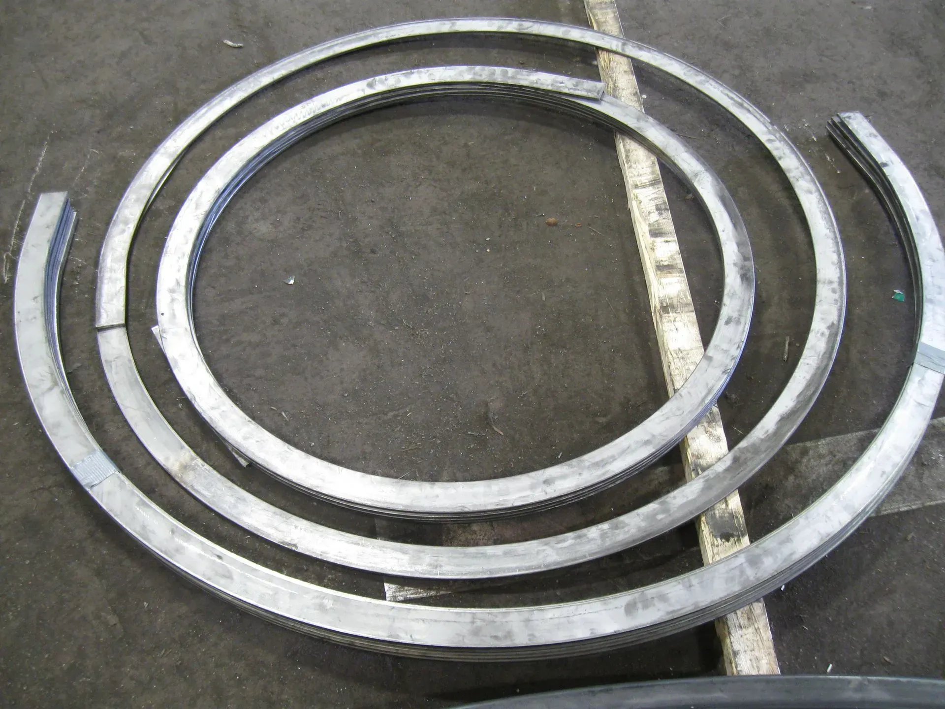 Three metal rings of different sizes arranged on a gray surface, possibly for construction or manufacturing.