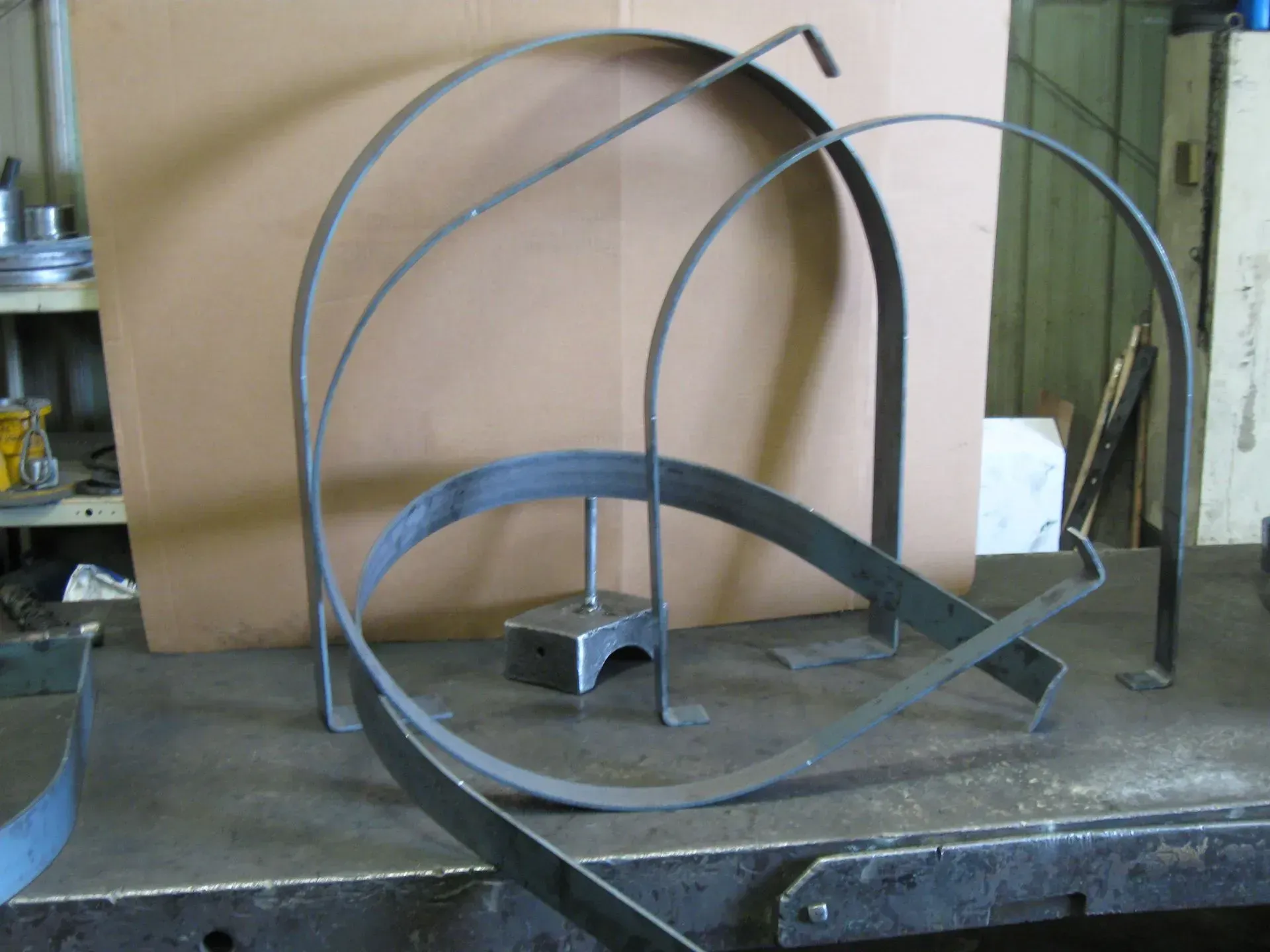Metal arcs and supports on a work surface, possibly for a structural project in a workshop.