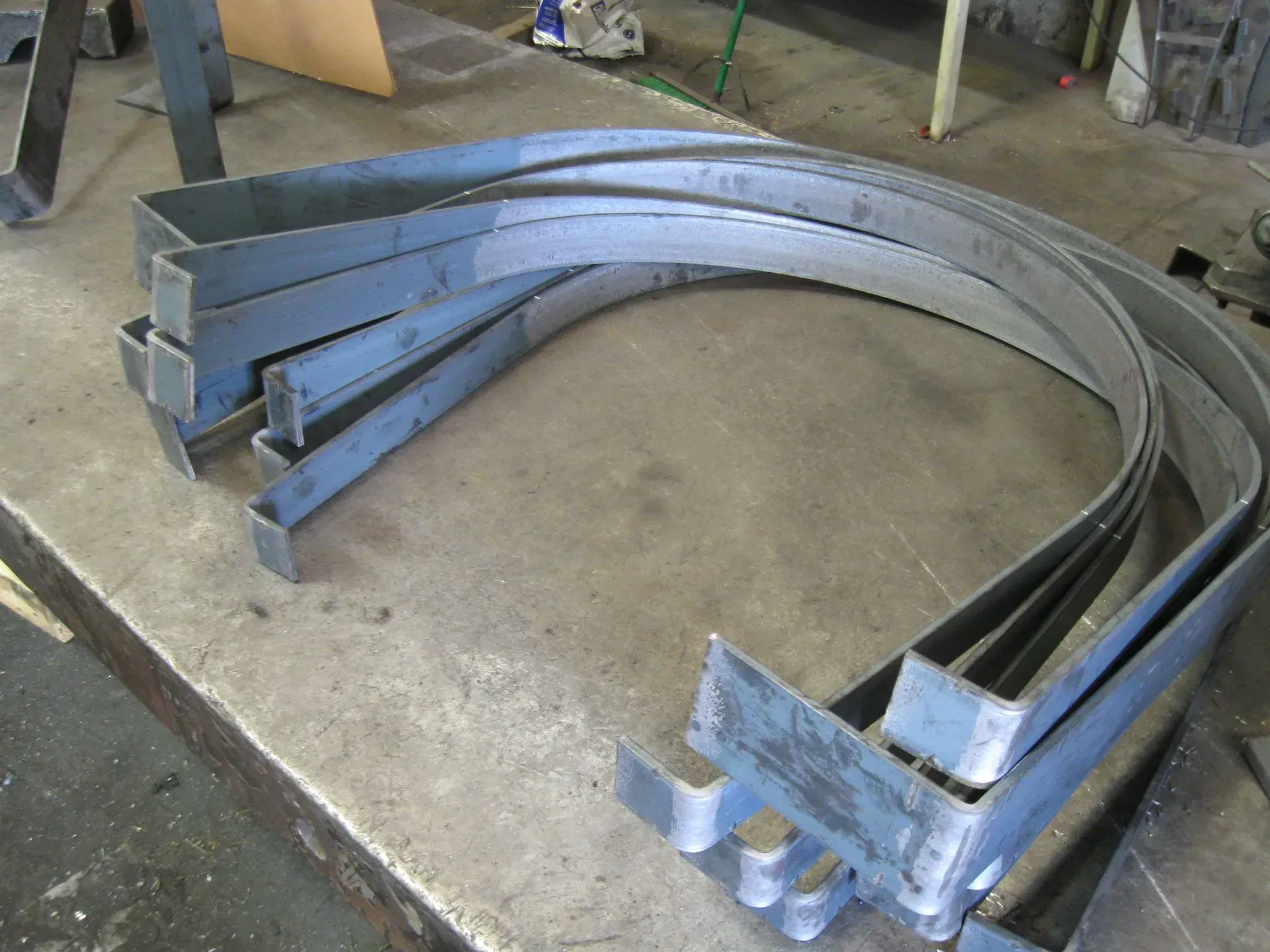 Metal, curved, U-shaped brackets stacked on a metal surface, in a workshop setting.