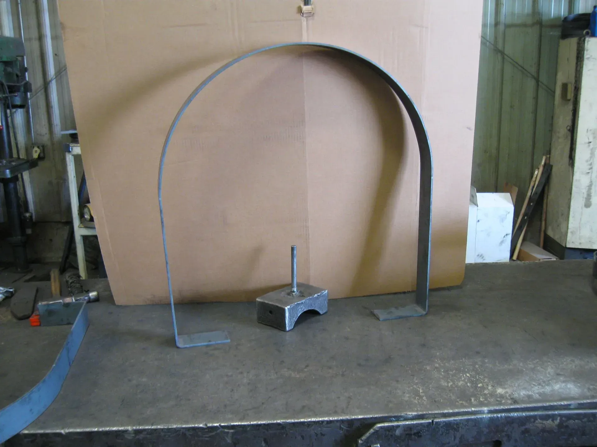 Metal arc frame with base and vertical supports on a steel table.