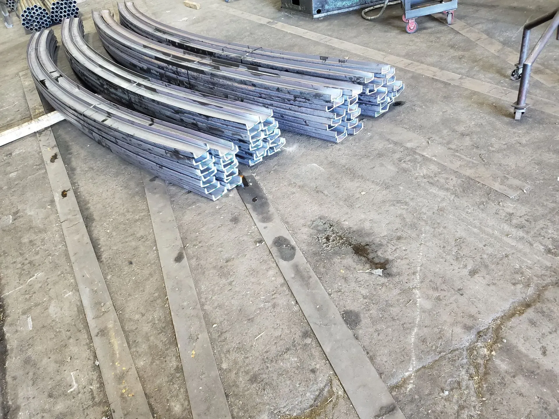 Curved metal beams stacked on a concrete floor in a workshop.