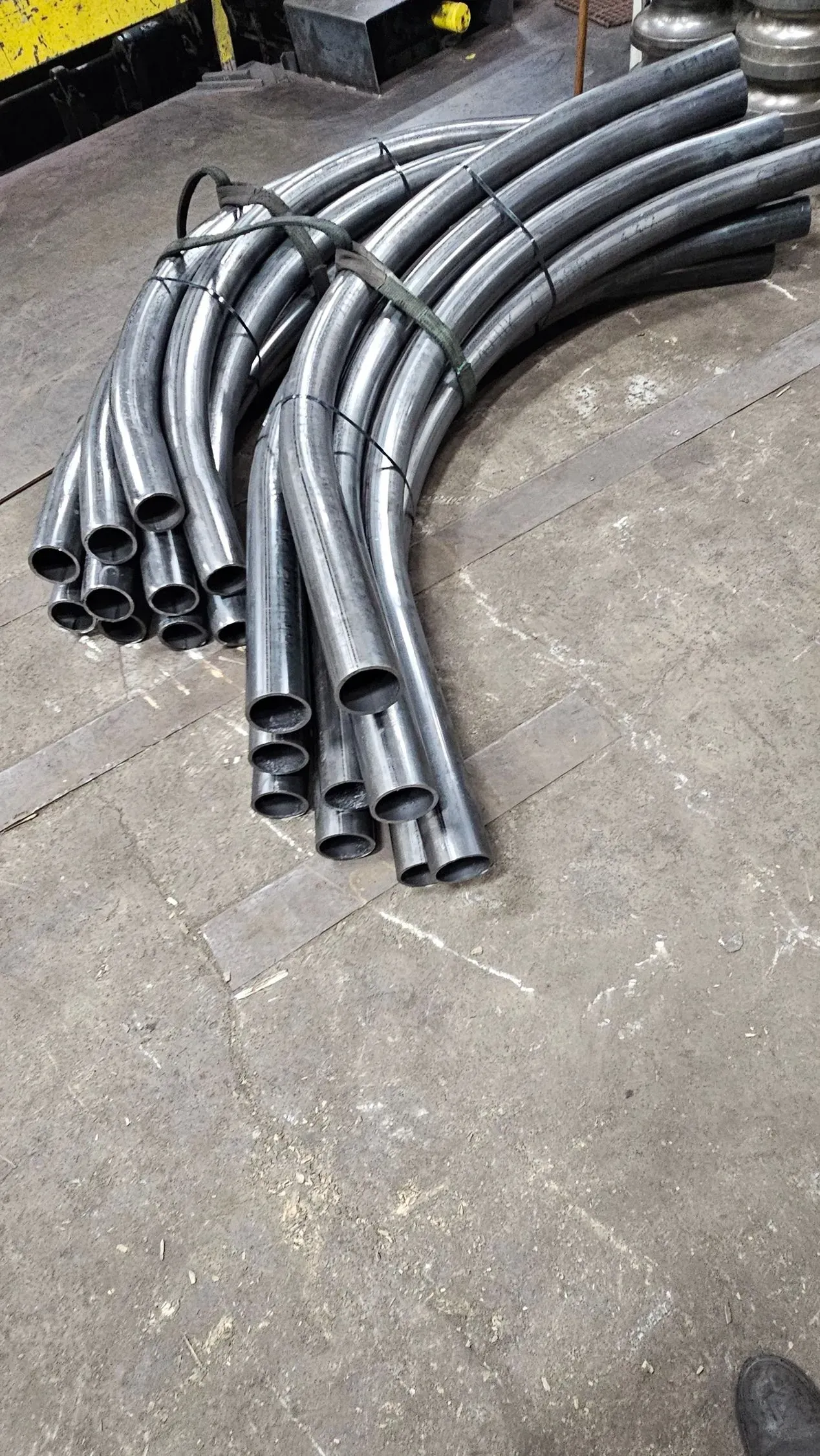 Bundle of bent metal pipes on a concrete floor, secured with a black band.