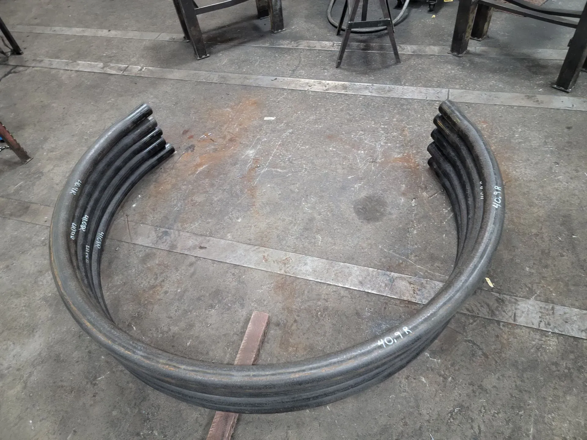Curved metal bars stacked in an arc on a shop floor.