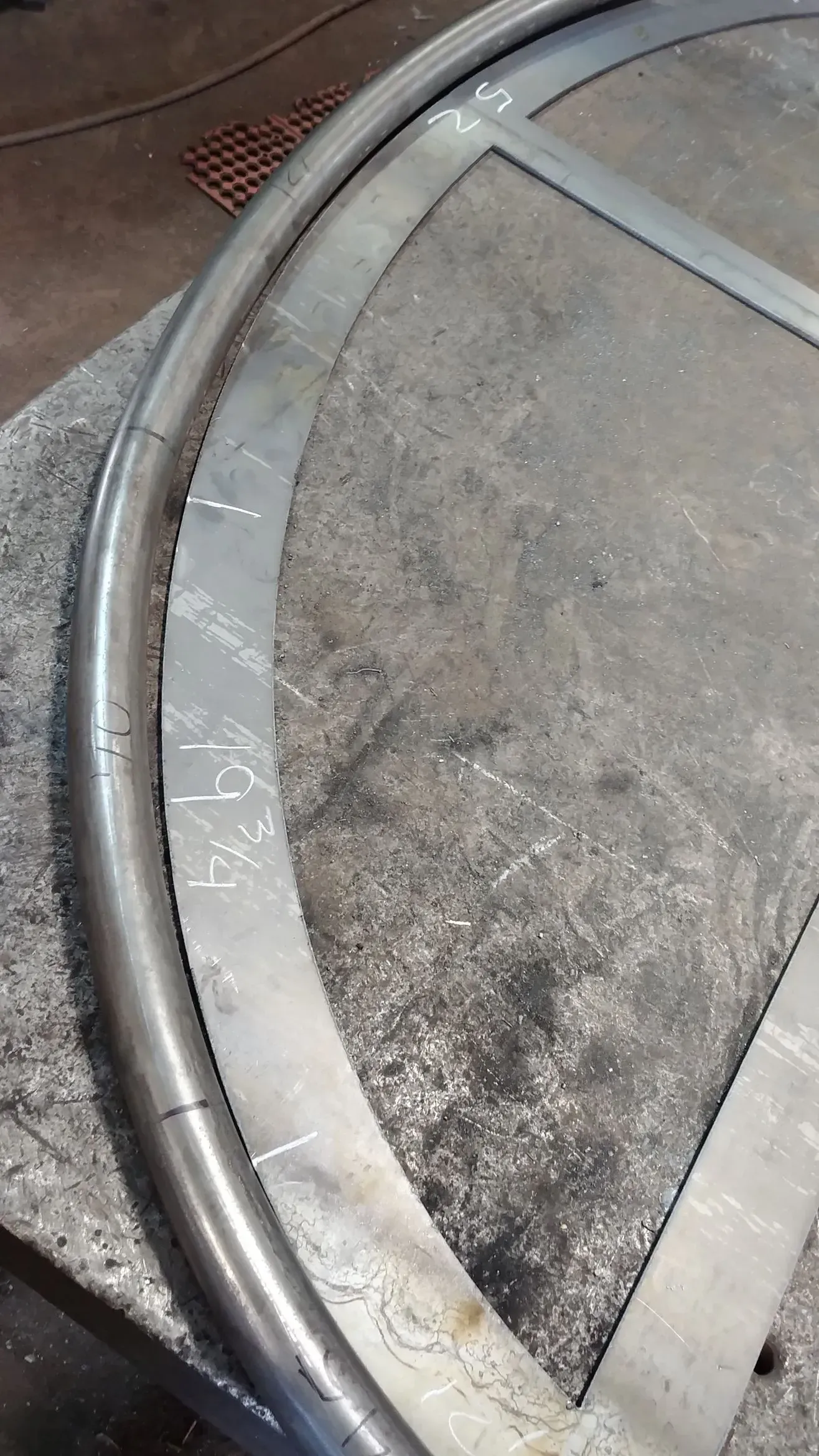 Metal frame under construction; curved tube next to cut metal pieces, marked with numbers.