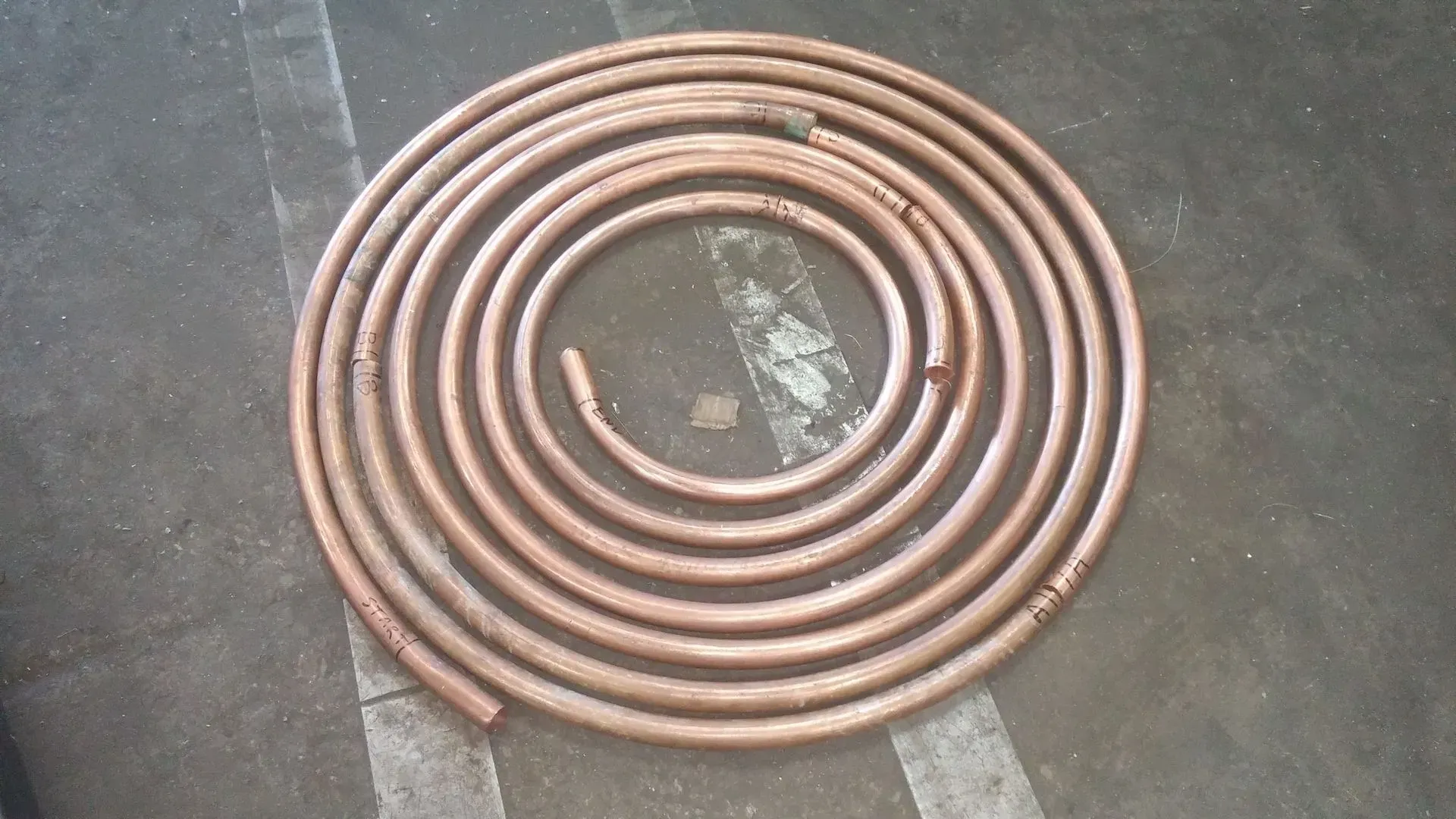 Coiled copper tubing on a gray surface, arranged in a spiral pattern.