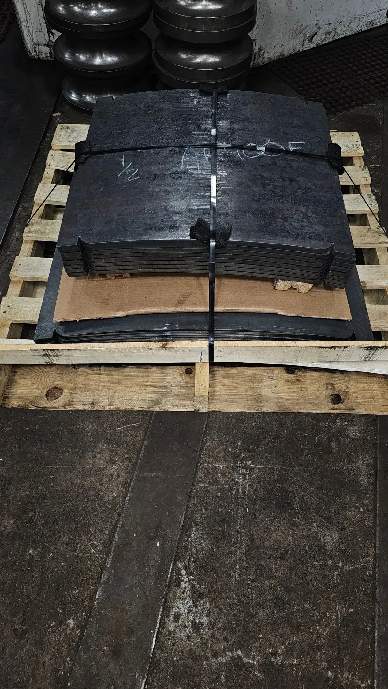 Black rubber sheets stacked on a wooden pallet; tires are in the background.