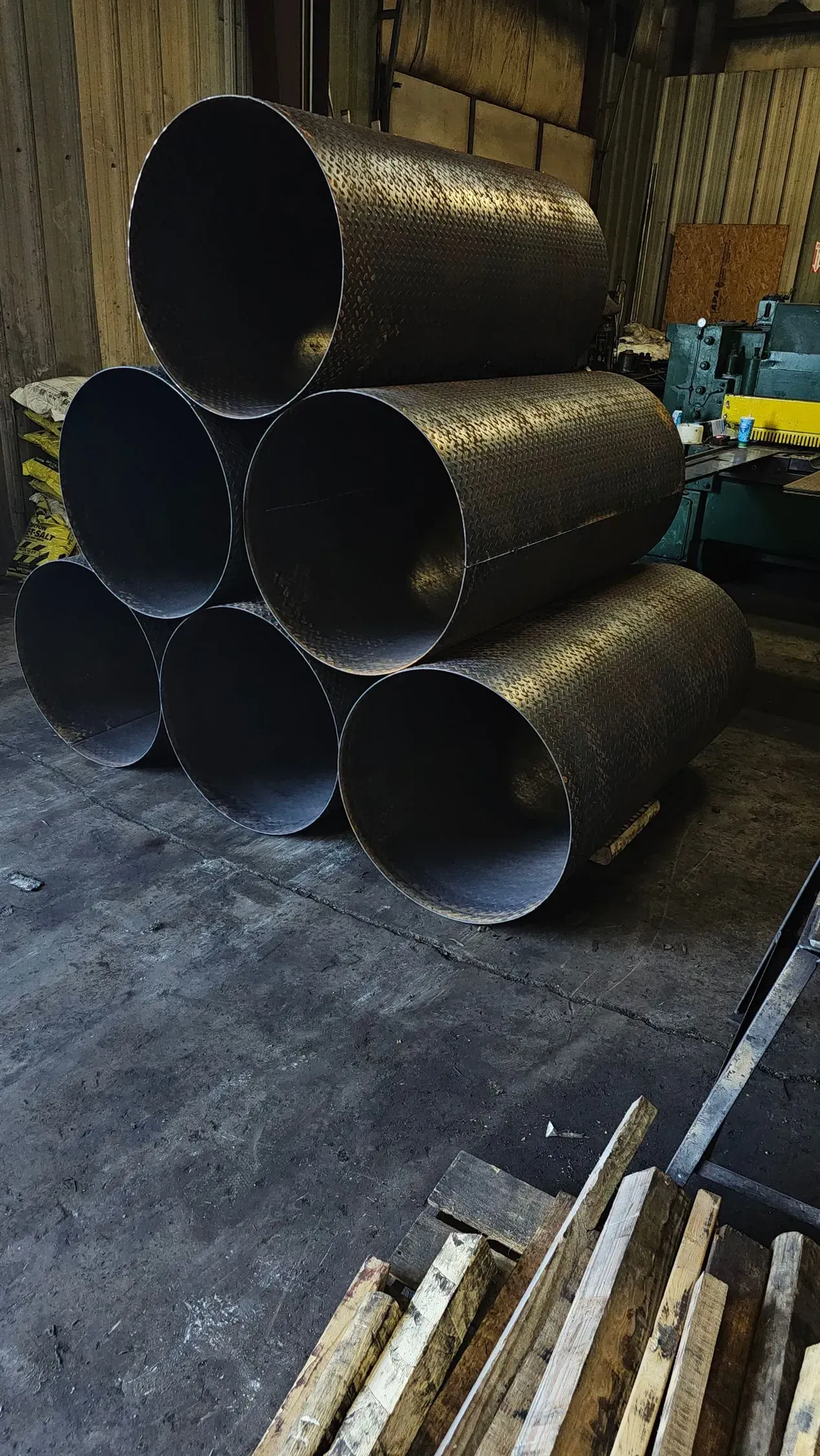 Six dark metal cylinders stacked in a triangular arrangement on a dusty floor.