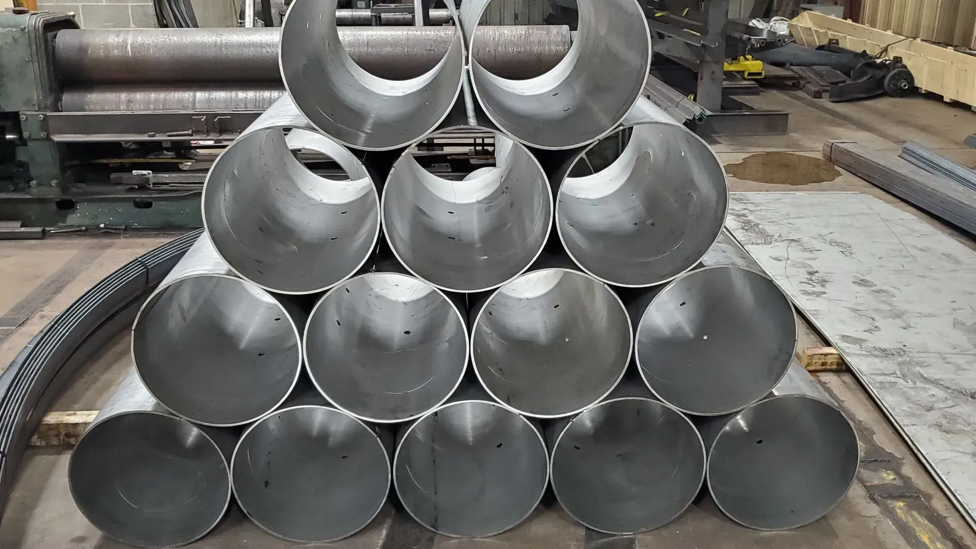 Stack of metal cylinders with angled openings, possibly pipes, in a workshop.