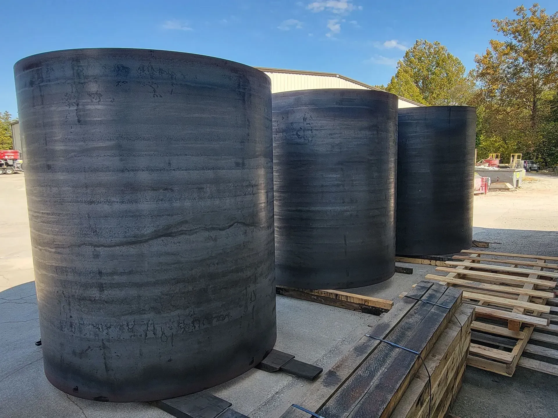 Three large, black cylindrical tanks on concrete, outdoors under a blue sky, with wood pallets nearby.