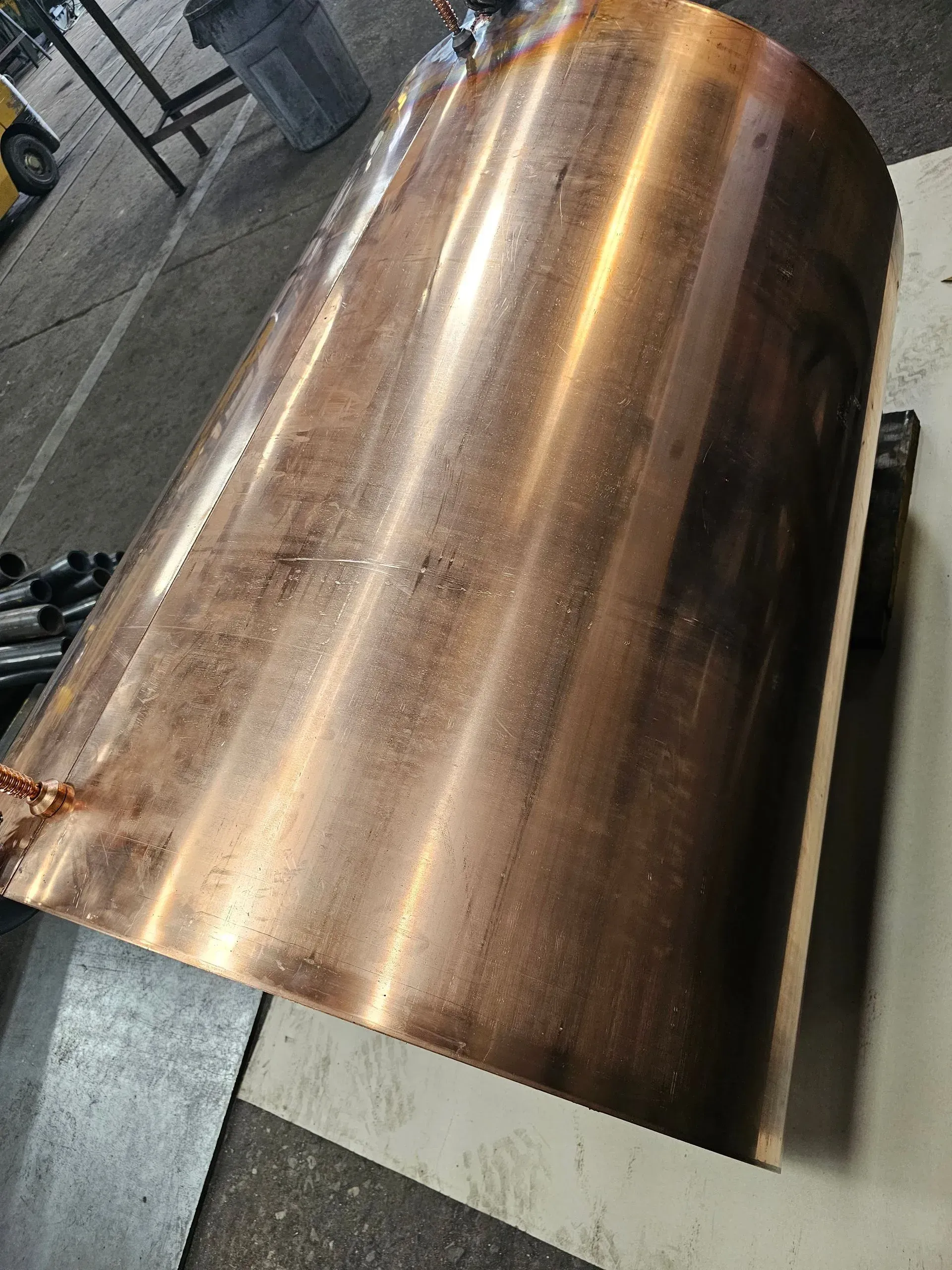 Copper cylinder, tapered, with brown patina, resting on a flat surface in a workshop setting.