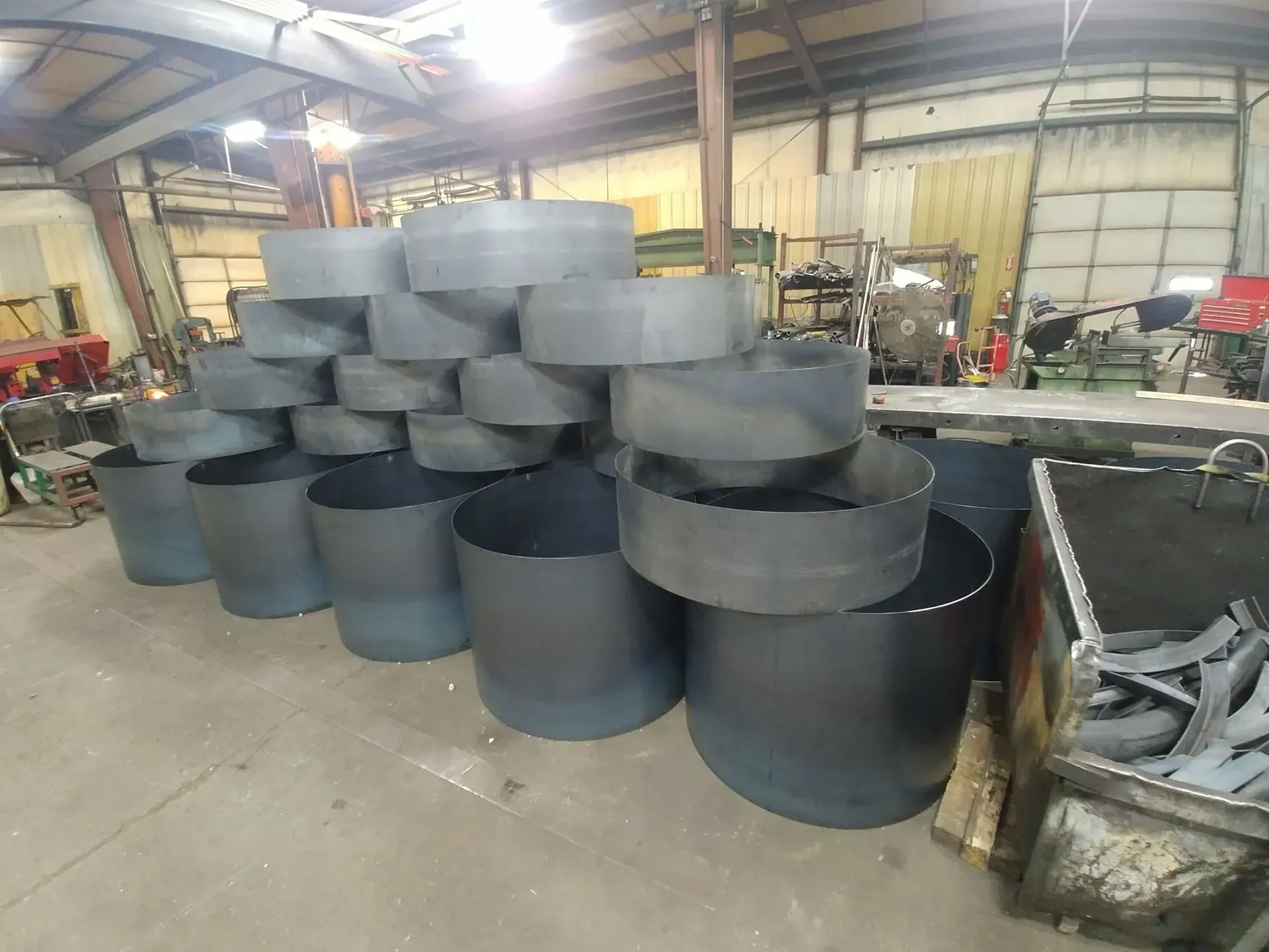 Metal cylinders and rings stacked in a warehouse. Gray metal, industrial setting.