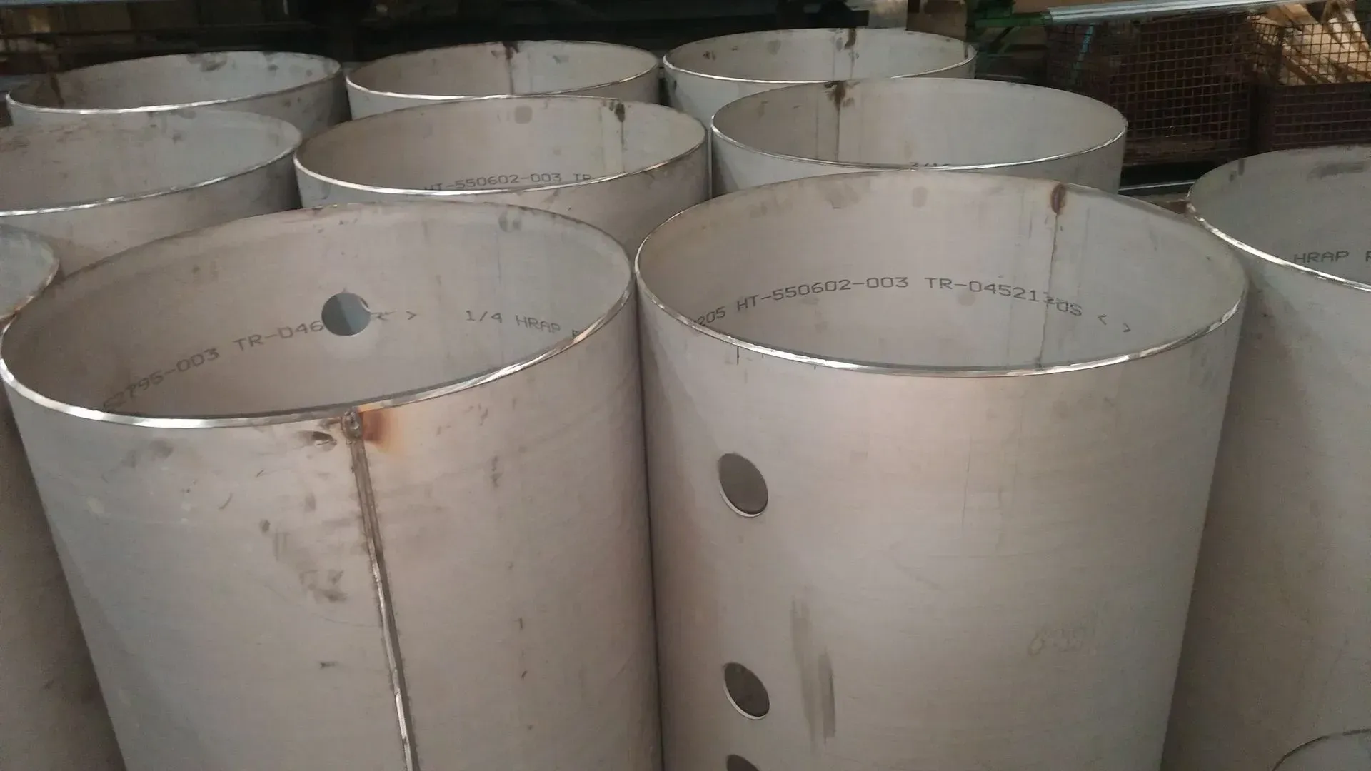 Cylindrical metal containers, possibly steel, stacked together. Each has a visible vertical seam and several small holes.