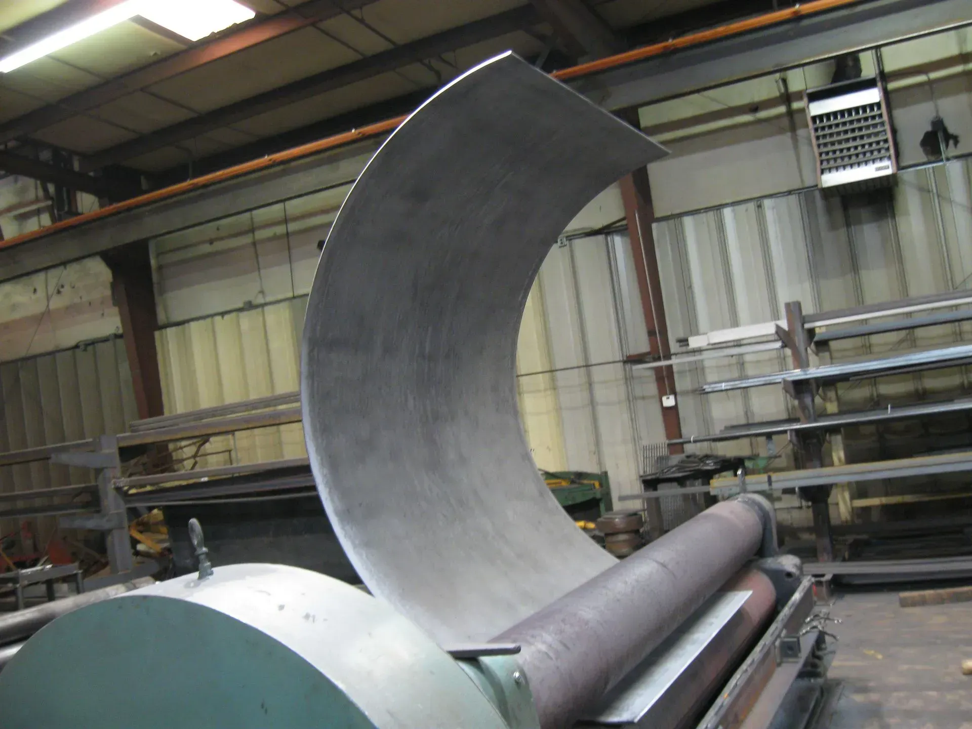 Metal sheet being curved on a roller machine inside a workshop.