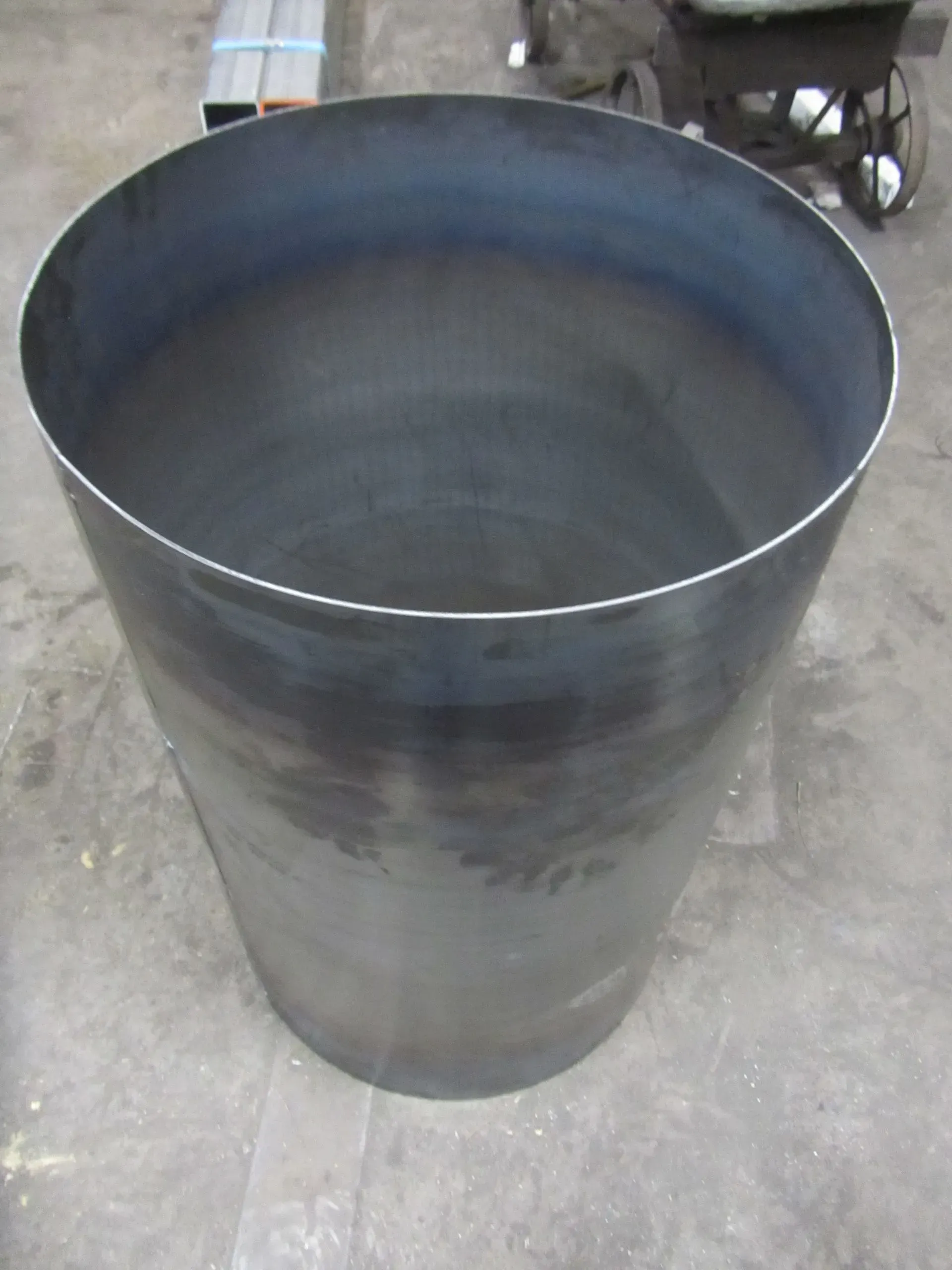 Large, open metal cylinder on a concrete floor, with a dark interior and a lighter rim.