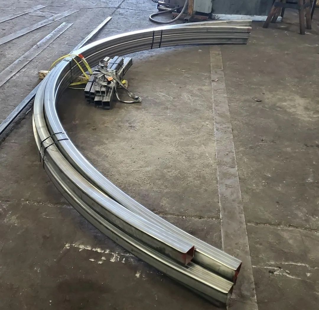 Curved metal beams stacked on a concrete floor in a workshop.