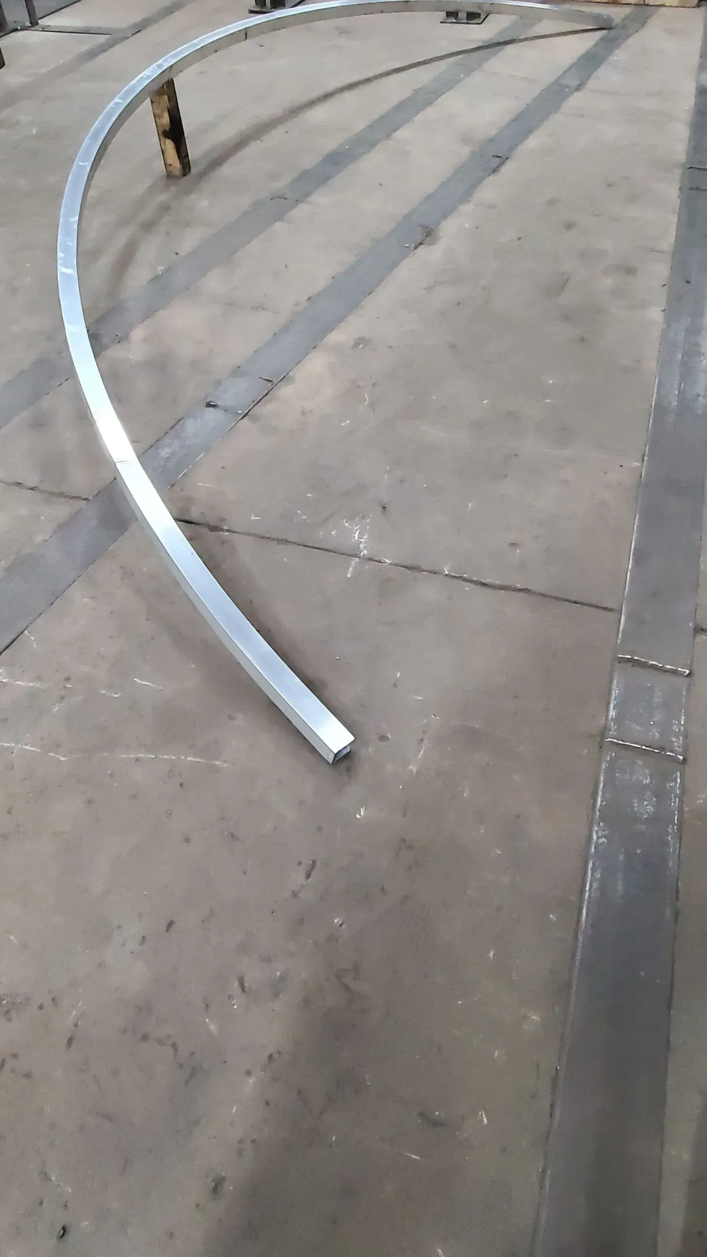 Curved, silver metal beam on a concrete floor in a workshop setting.