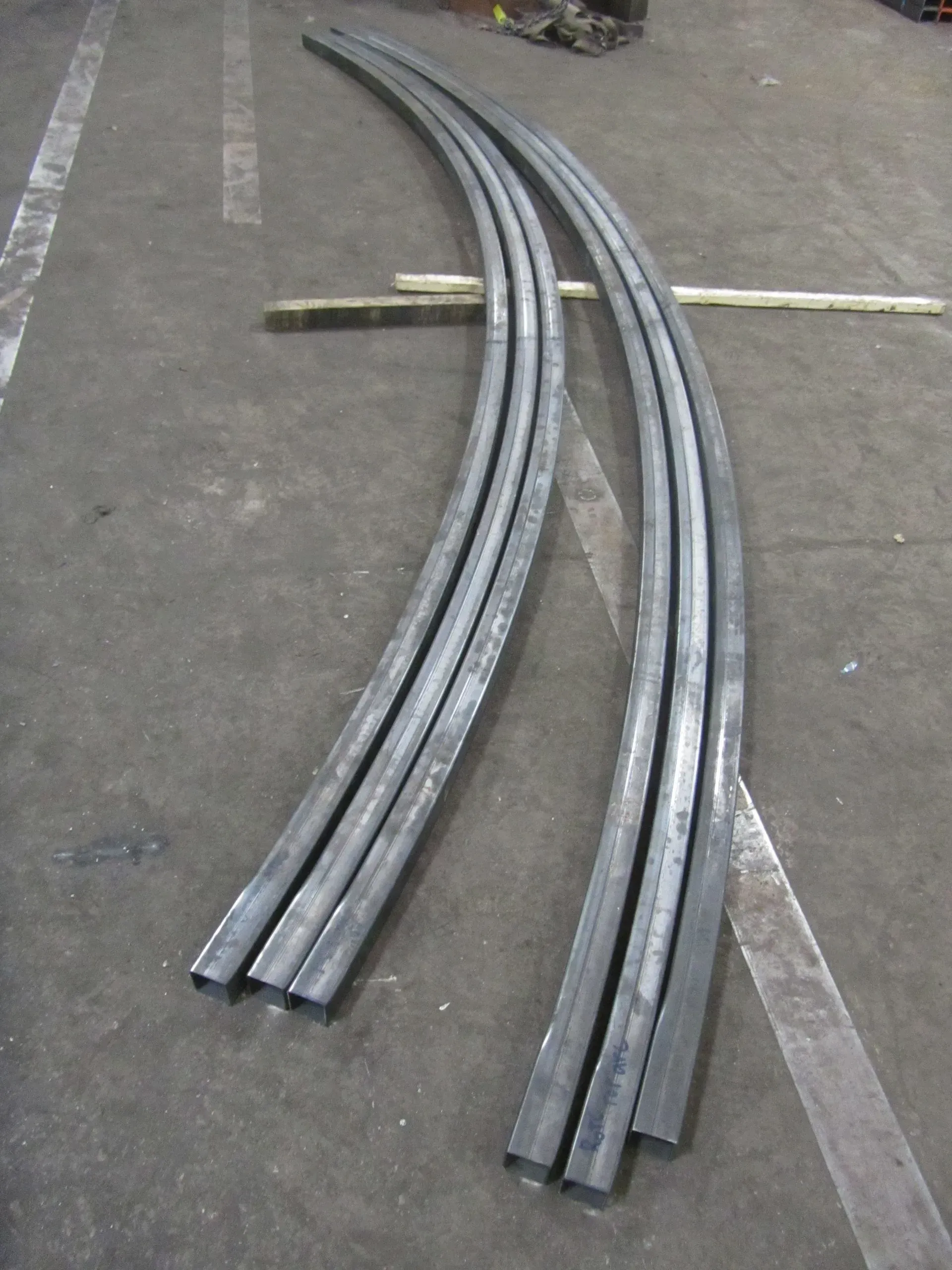Curved, gray metal beams on a gray concrete floor, possibly for construction or architecture.