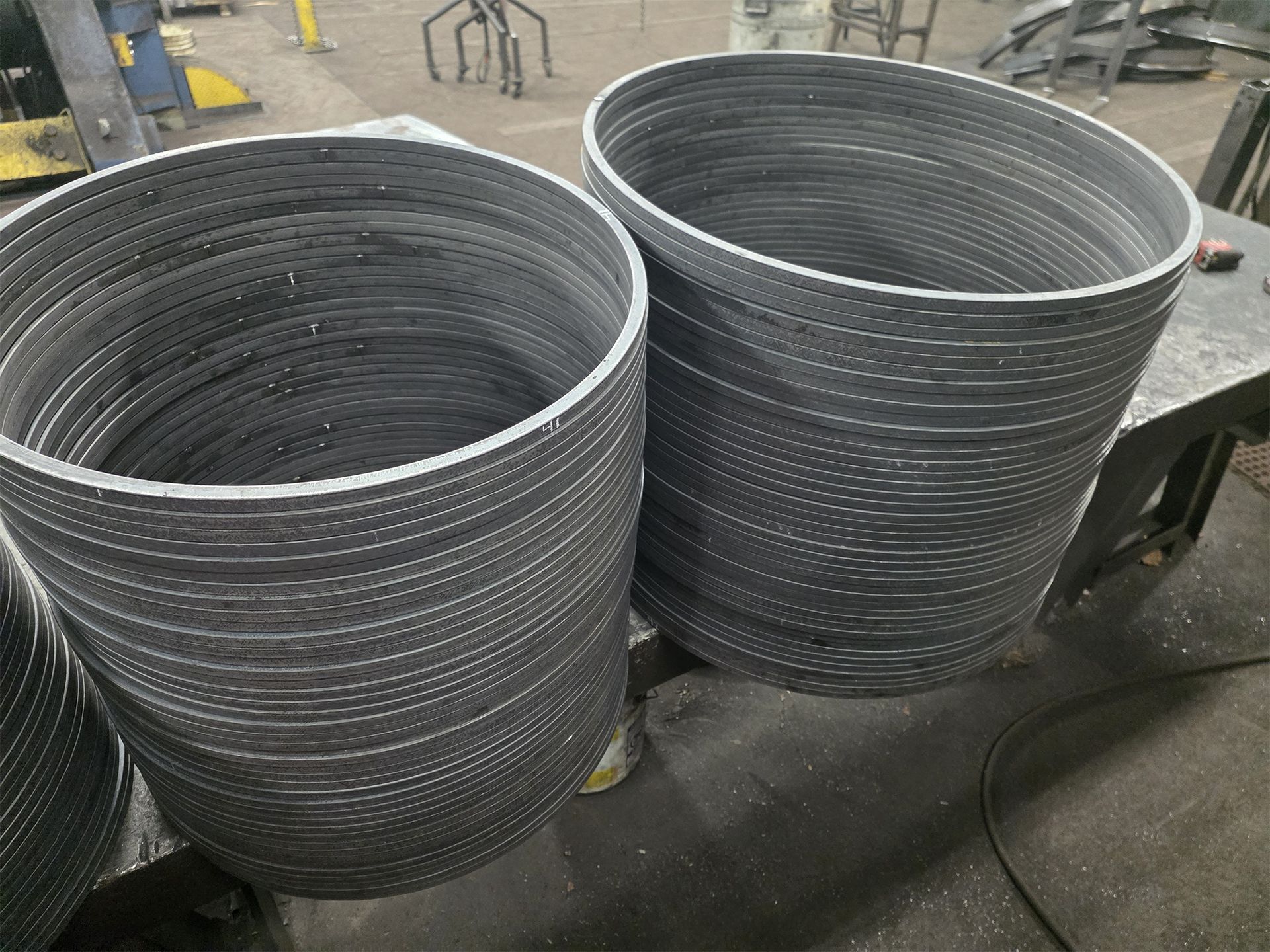 Two stacks of cylindrical metal tubes with horizontal slits, inside a workshop.