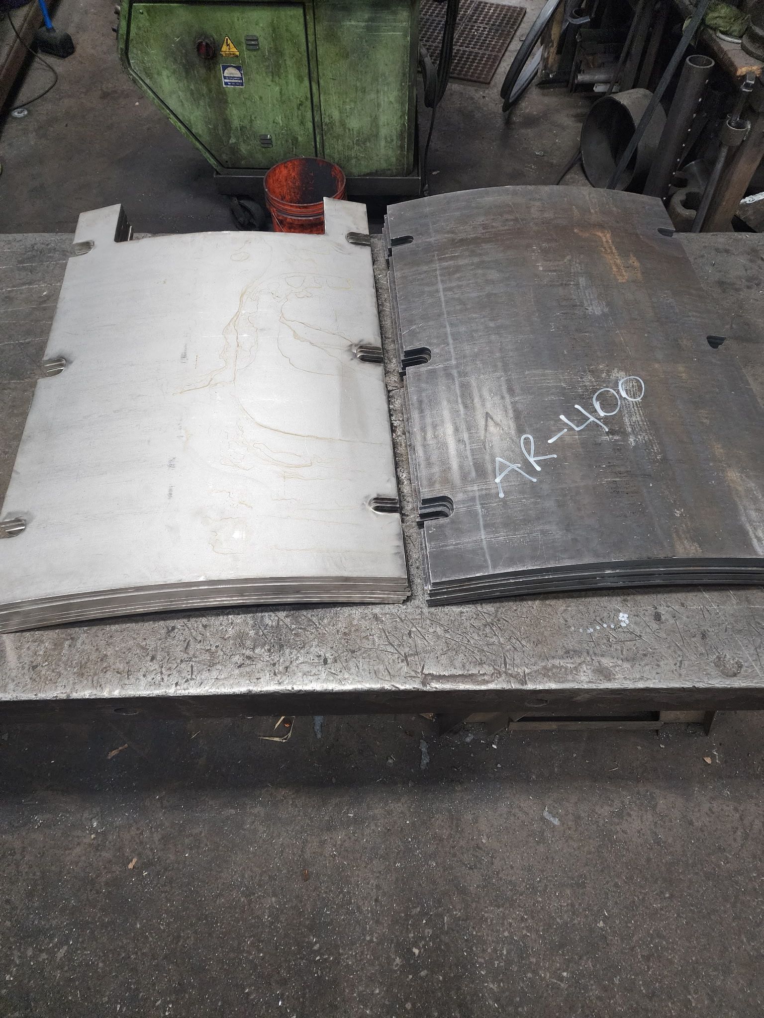 Two metal plates, one shiny and one dark, on a workbench in a workshop.