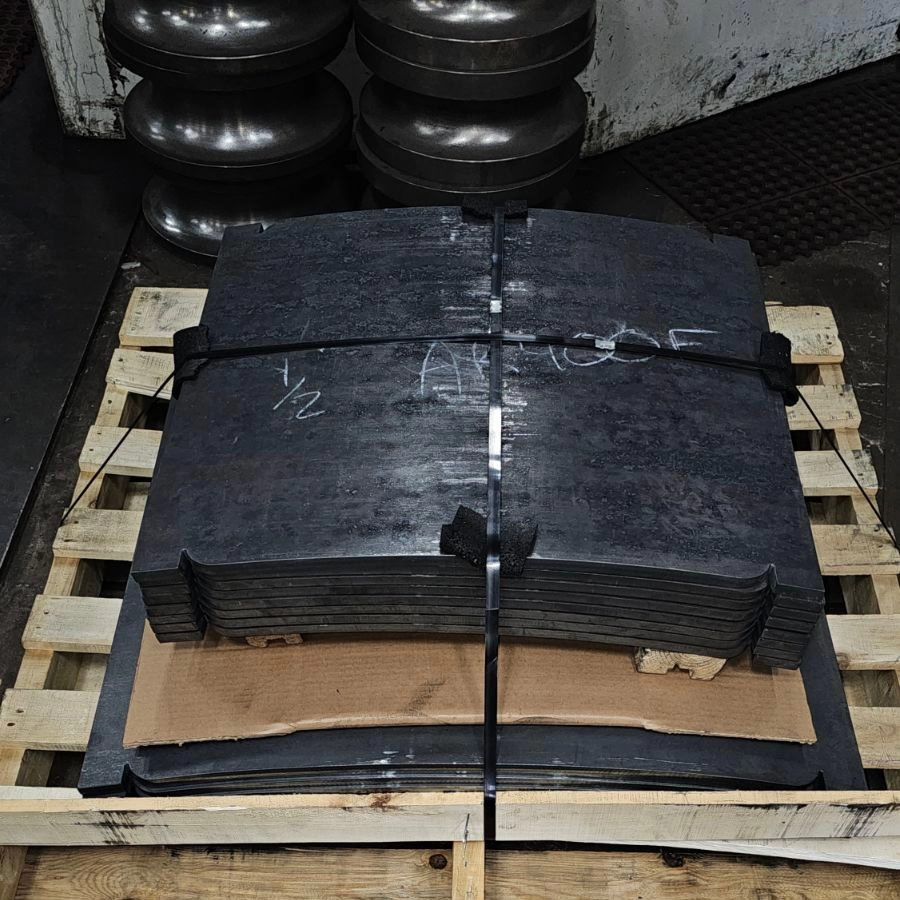 Stack of black metal sheets strapped to a pallet in a warehouse, with labeling and industrial rollers in the background.