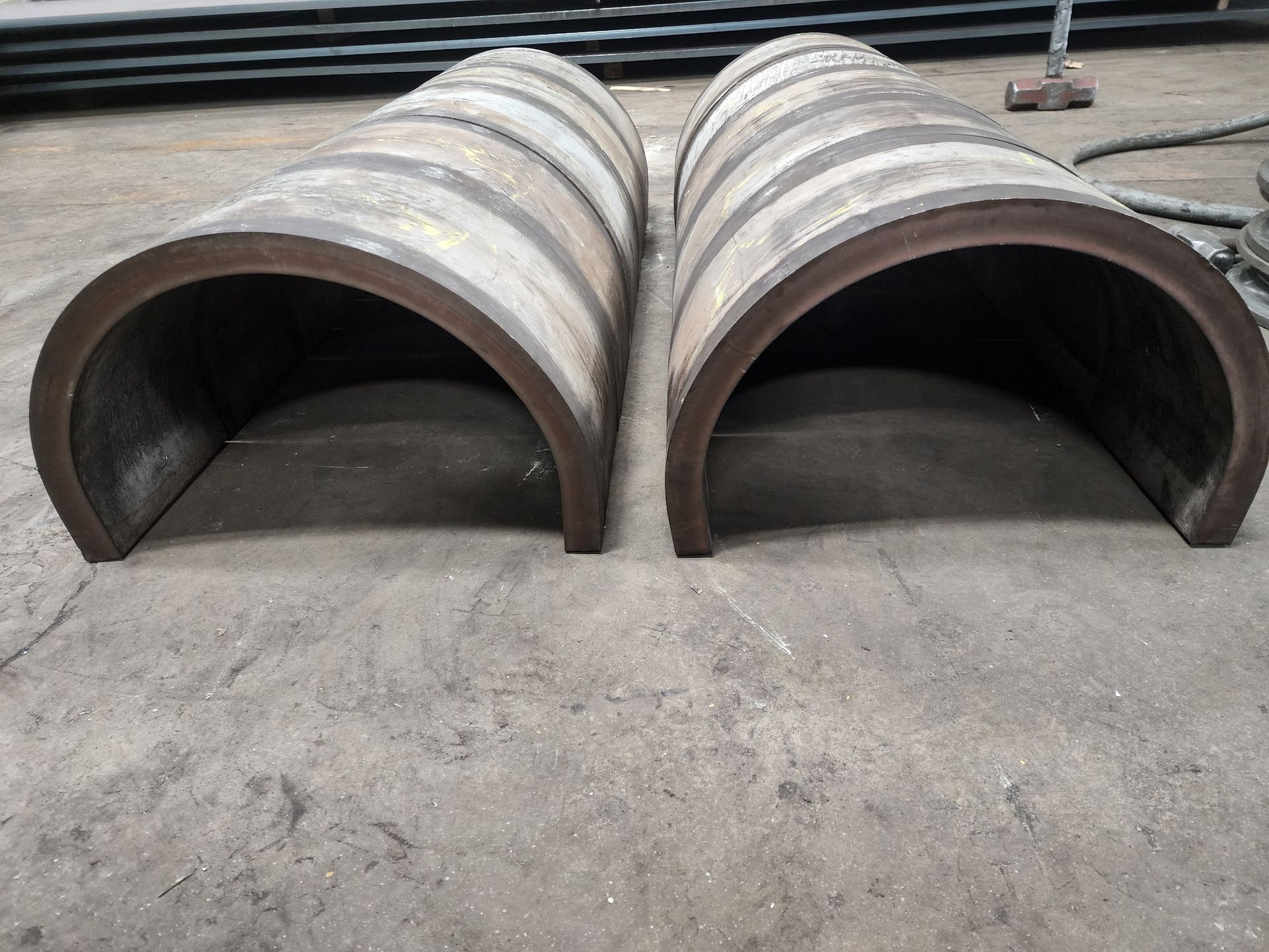 Two large, semi-circular metal pieces, side-by-side, resting on a concrete floor.