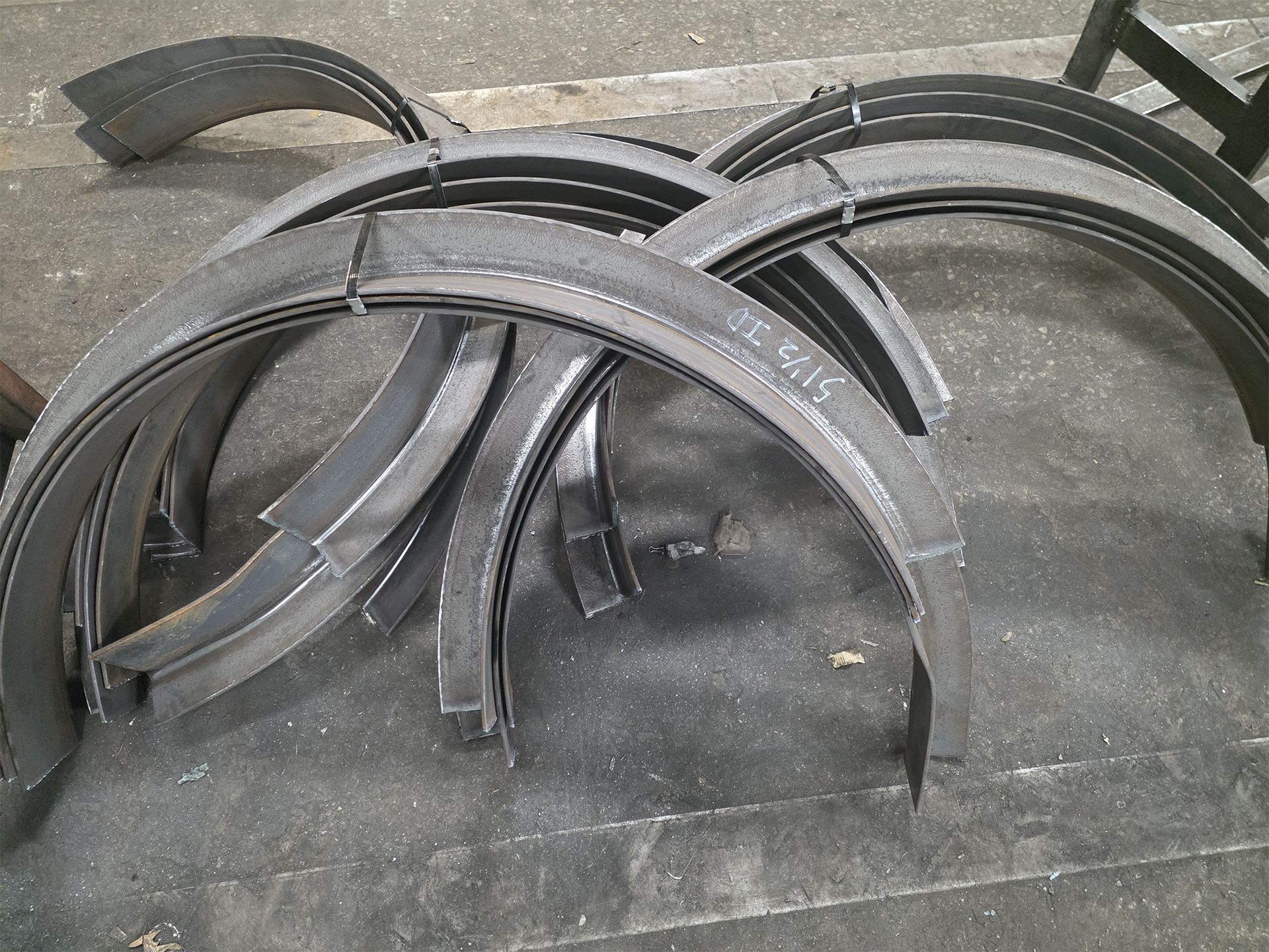 Curved metal pieces arranged on a dark surface, possibly for construction or fabrication.