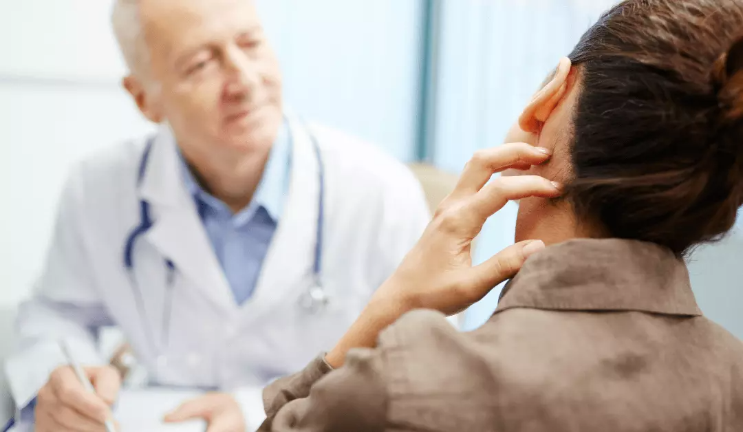 Doctor examining patient in office, speaking with a woman holding her head in discomfort