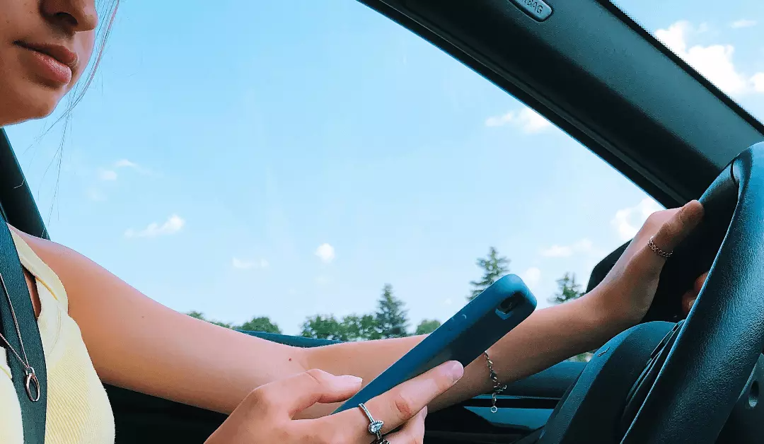 Driver holding a smartphone while steering a car on a sunny day