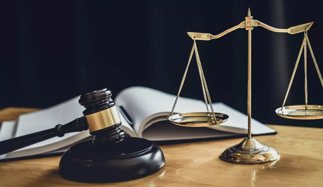 Judge's gavel, brass balance scale, and law books on a desk in a legal setting