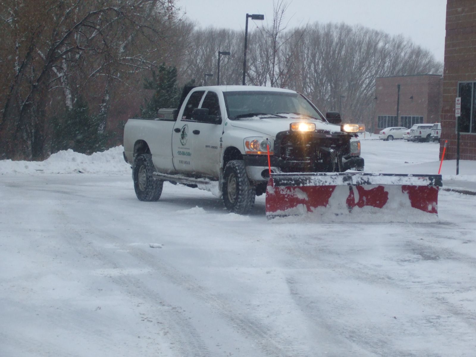 White snowplow truck clearing snow from a parking lot on a snowy day.