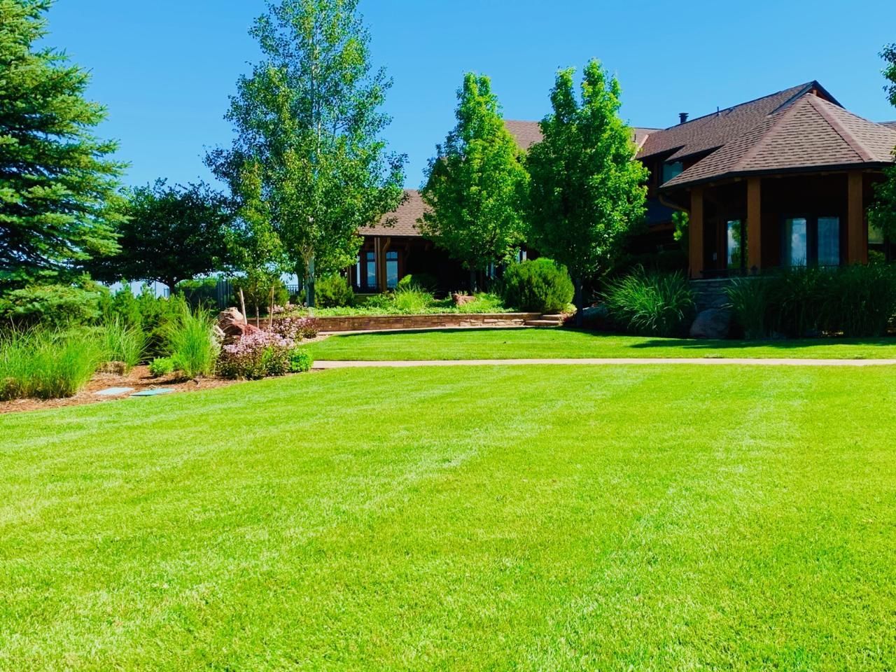 Green lawn in front of a large house with trees and landscaping, under a blue sky.