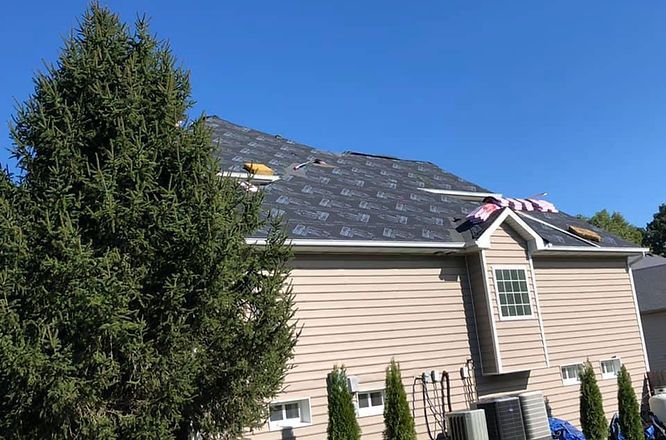 A house with a roof that is being installed and a tree in front of it.