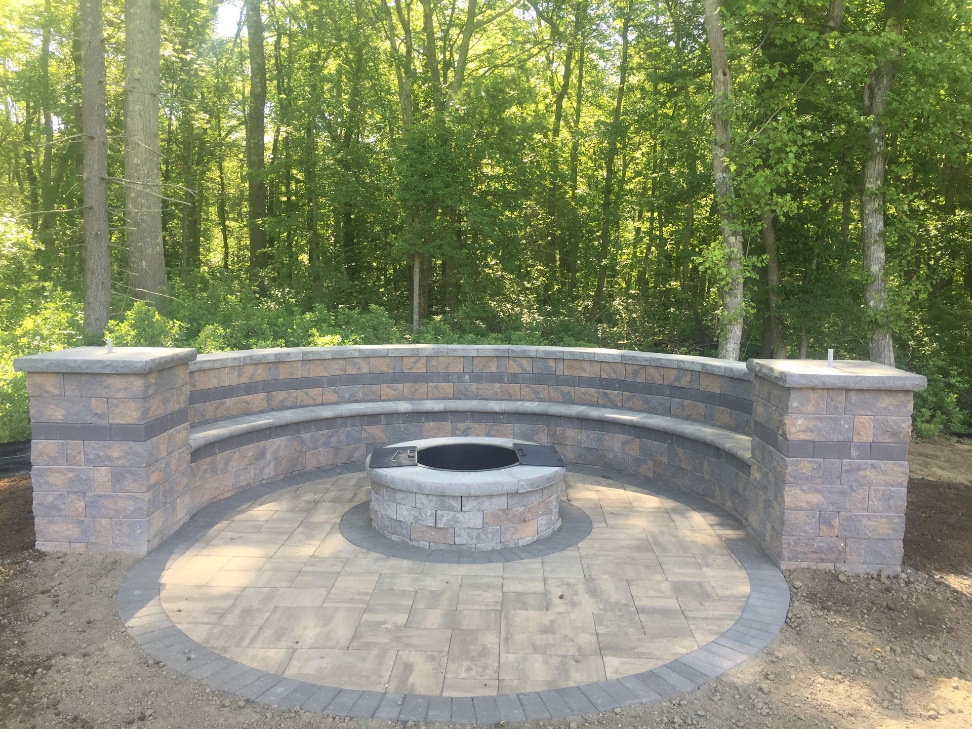 A fire pit is surrounded by a brick wall in the middle of a forest.
