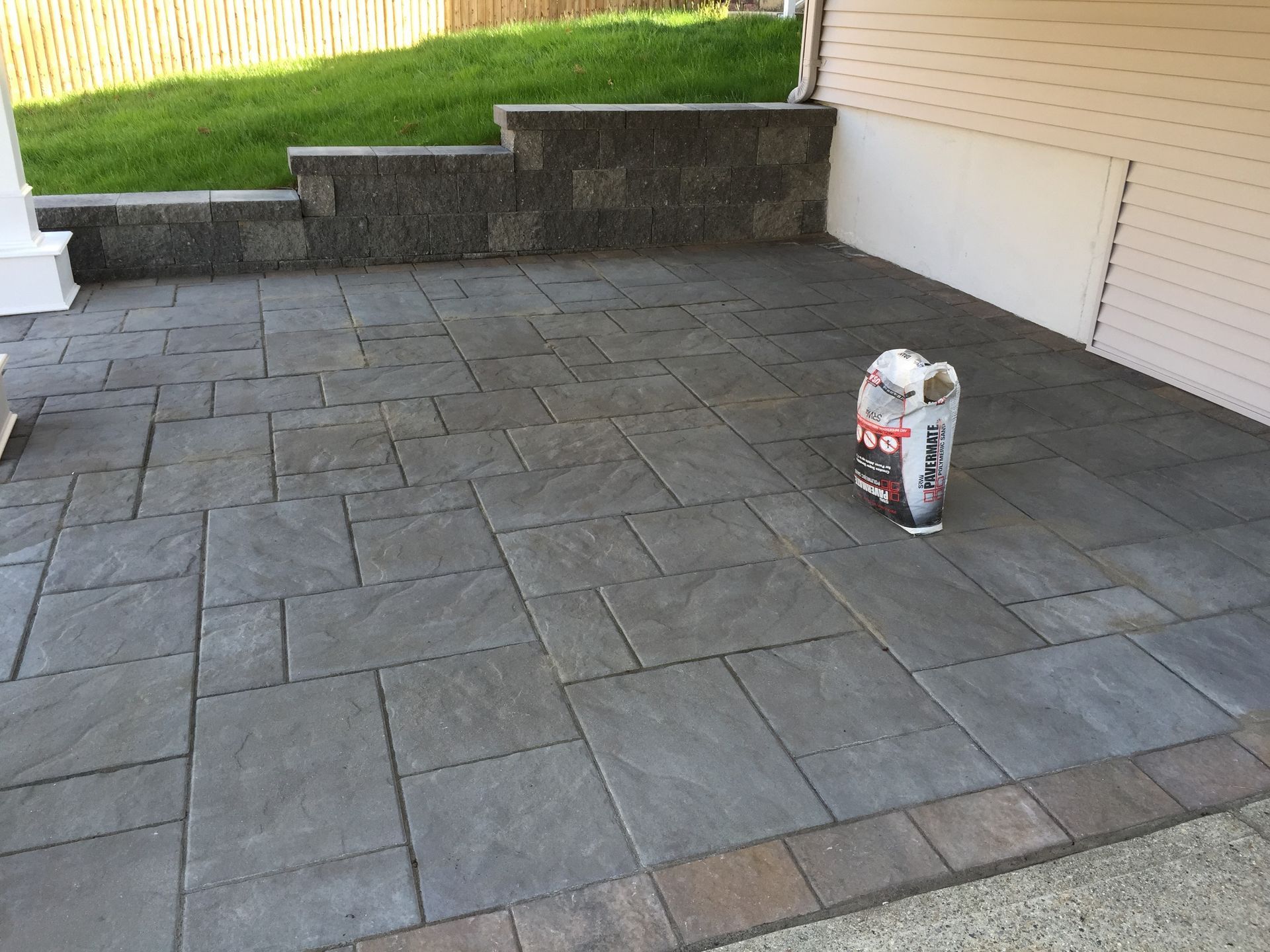 A bag of concrete is sitting on a patio next to a house.