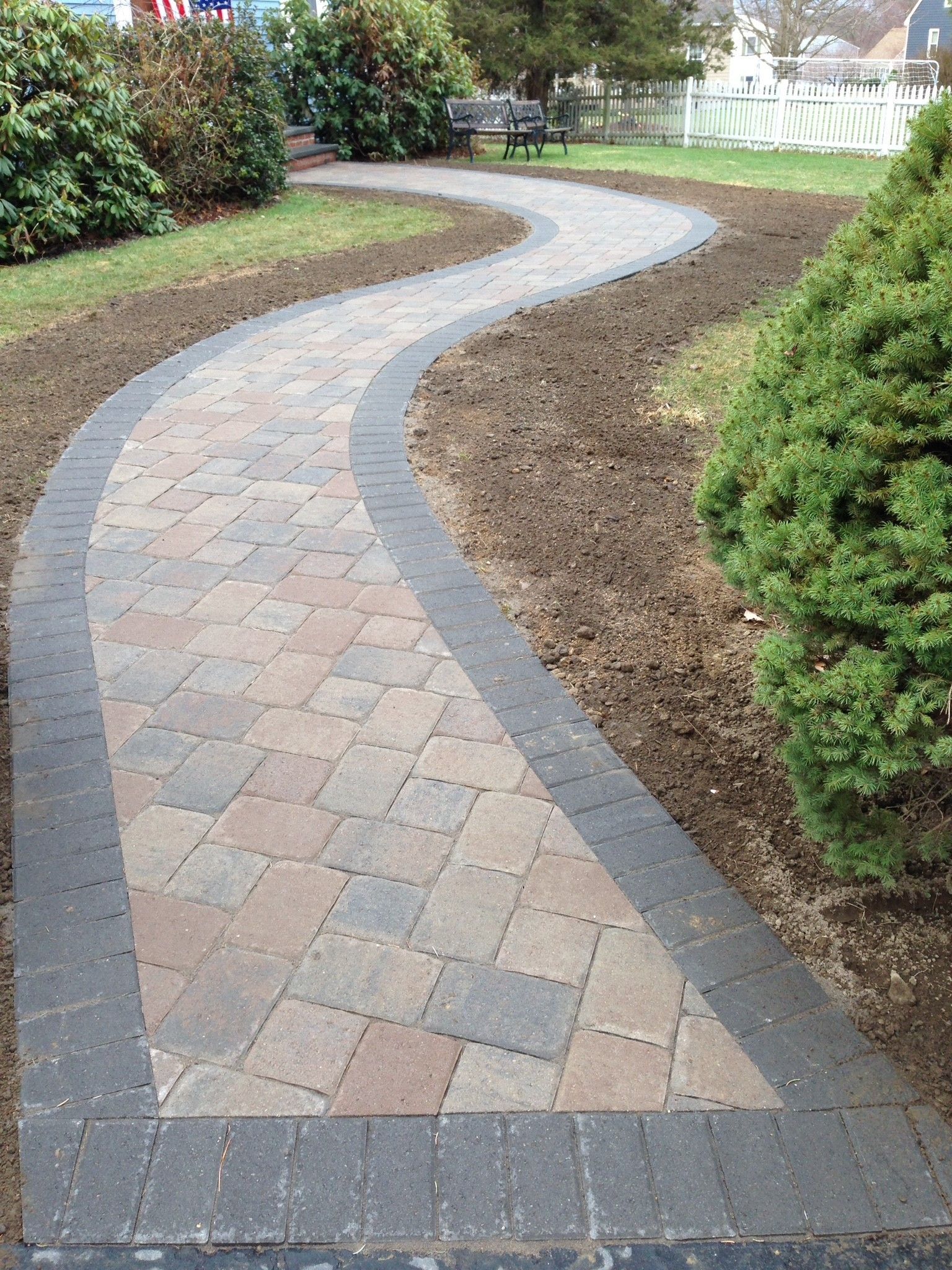 A brick walkway in a park with a bench in the background