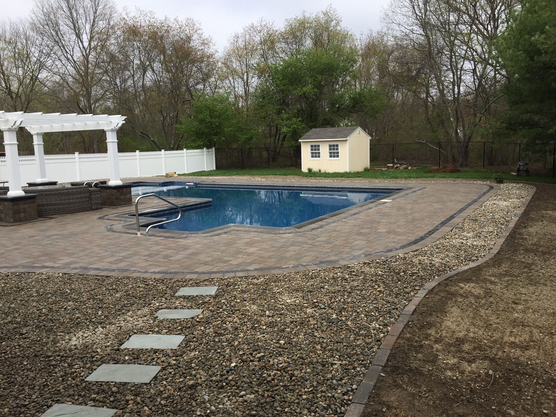 A large swimming pool in a backyard with a shed in the background.