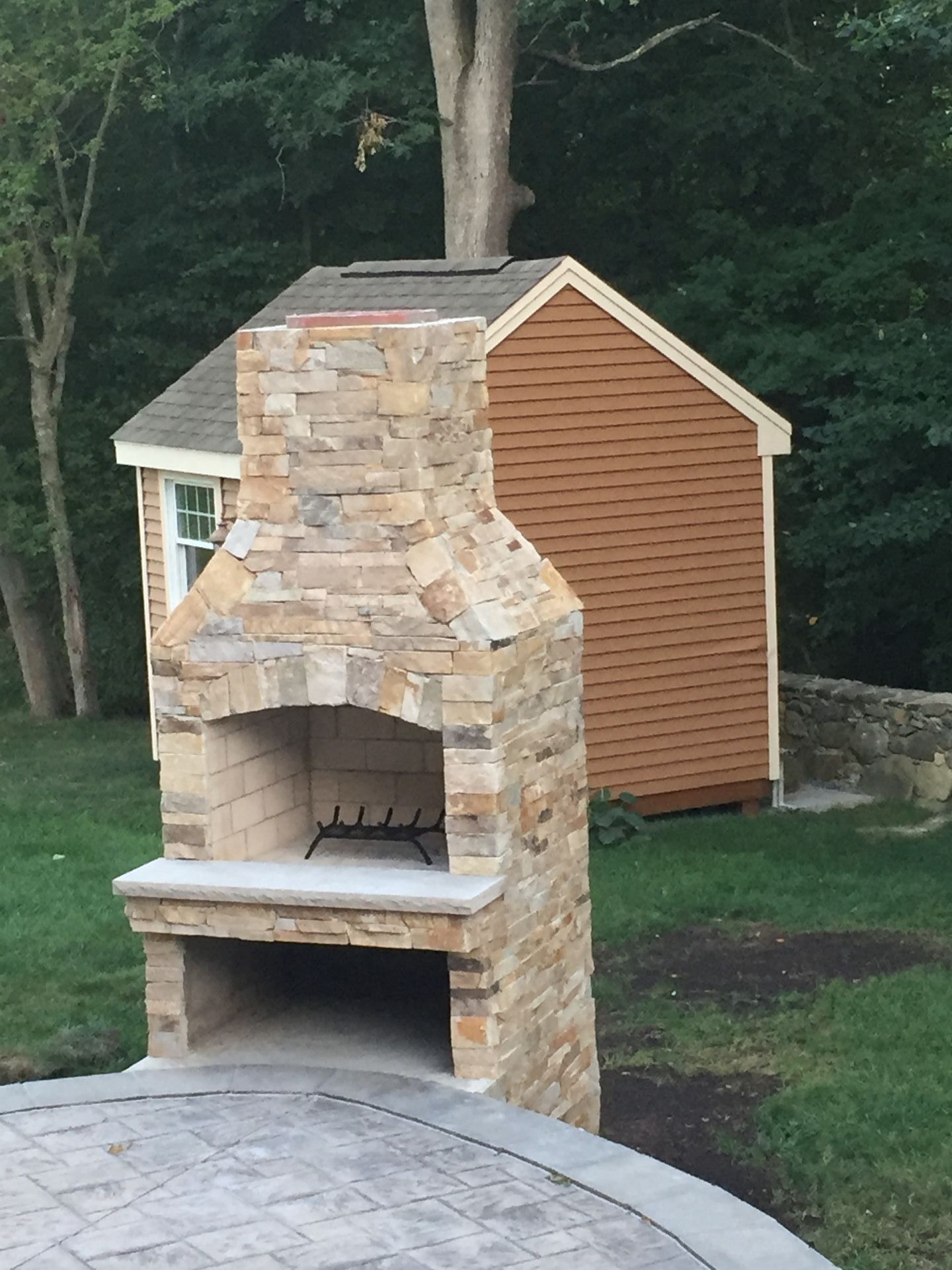 A stone fireplace with a shed in the background