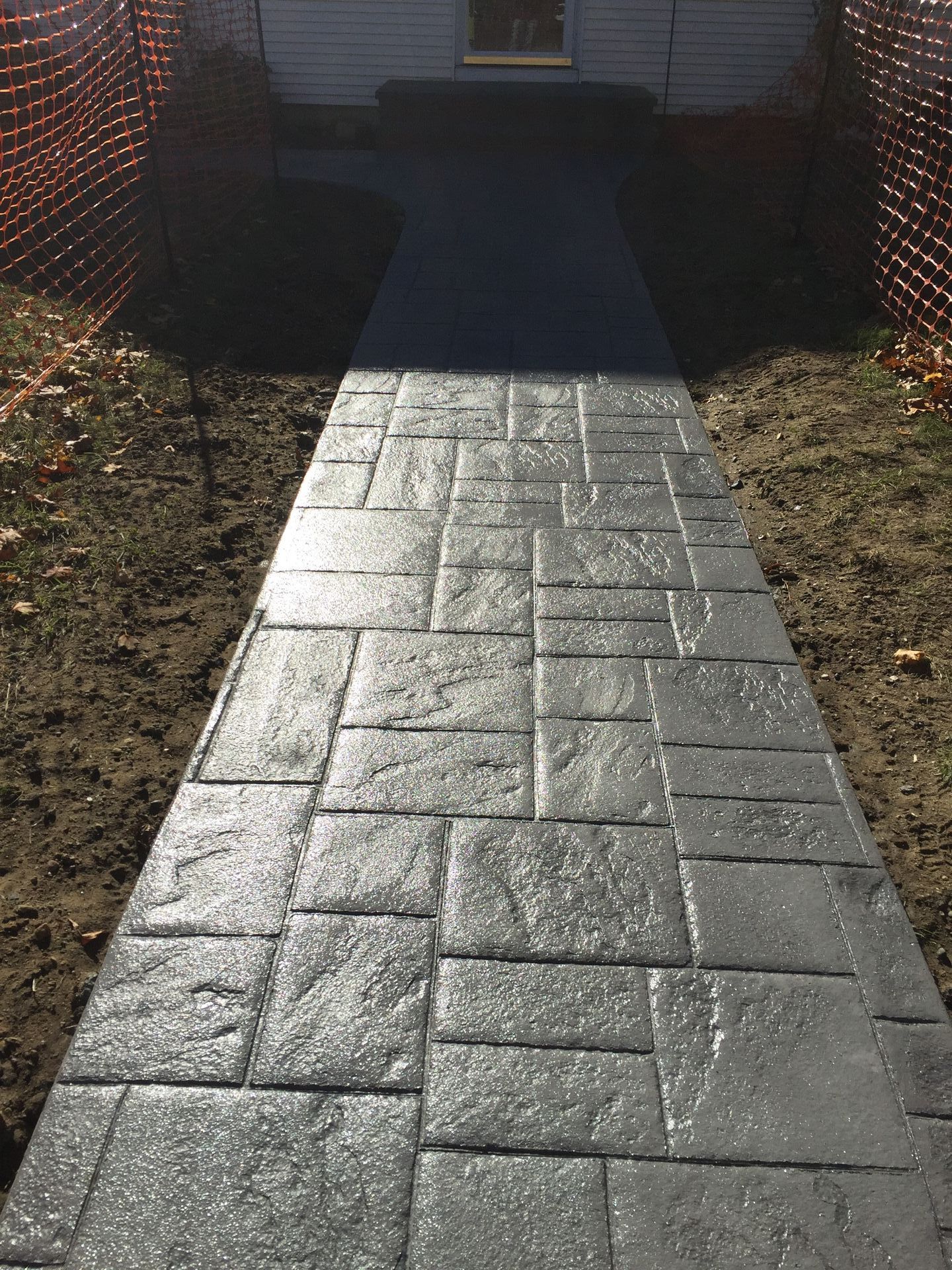 A concrete walkway leading to a house with a fence in the background.