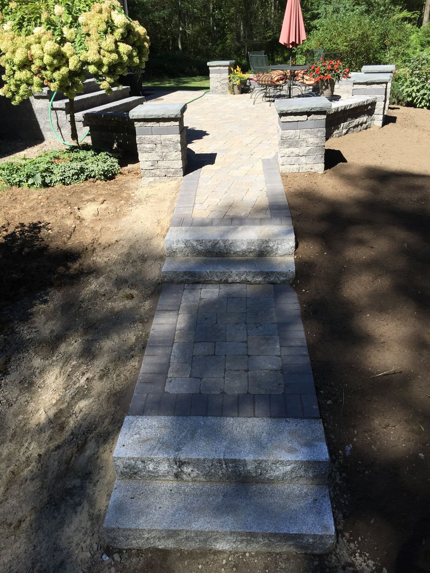 A brick walkway leading to a patio with a red umbrella in the background.
