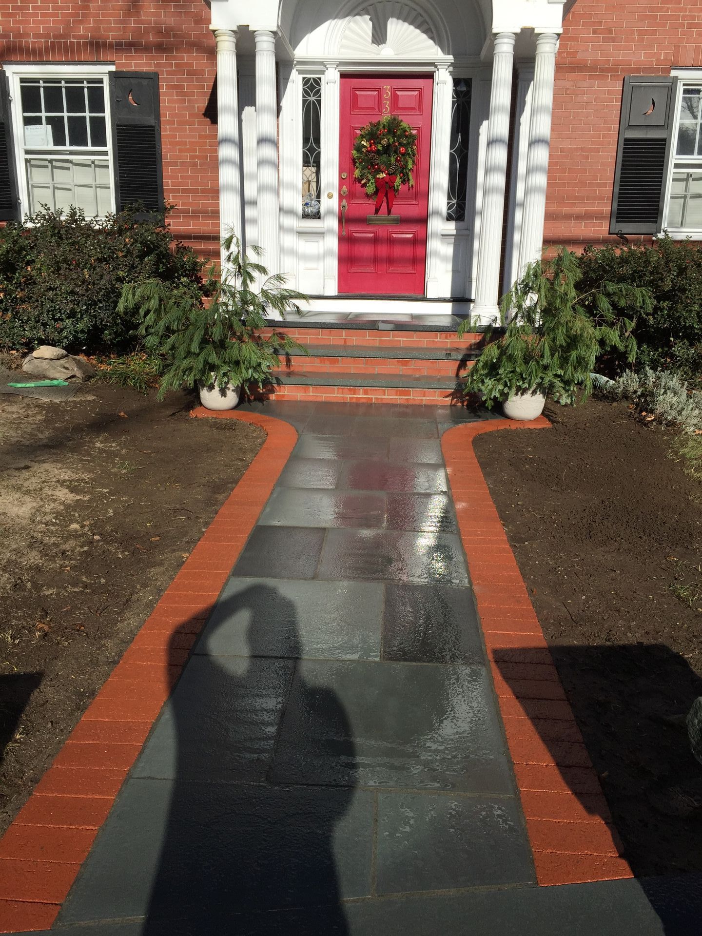 A brick walkway leading to a red door with a wreath on it