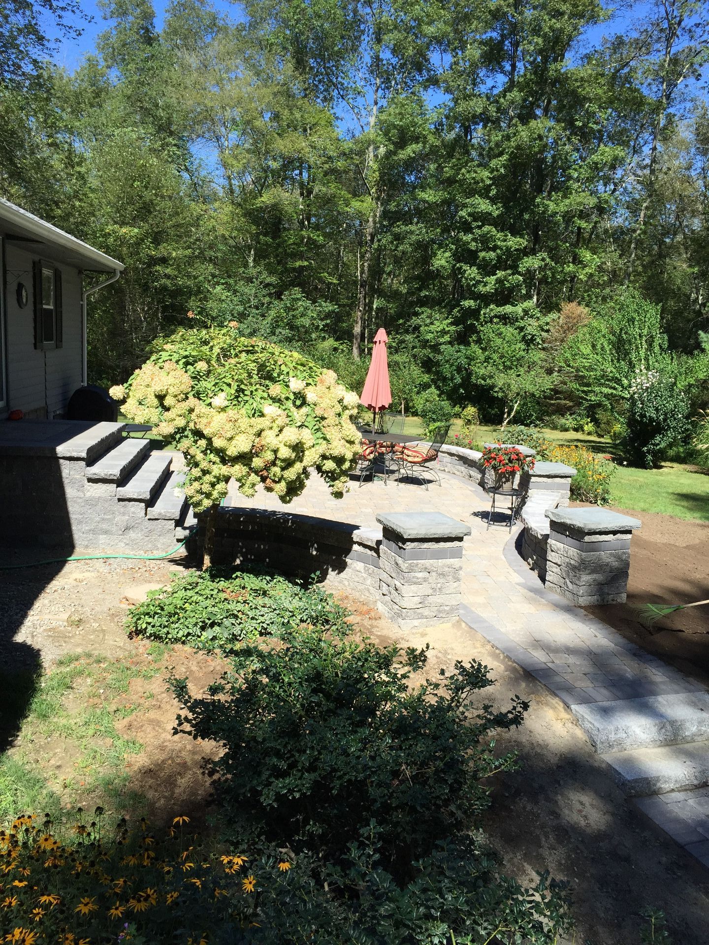 There is a patio with a red umbrella in the backyard.