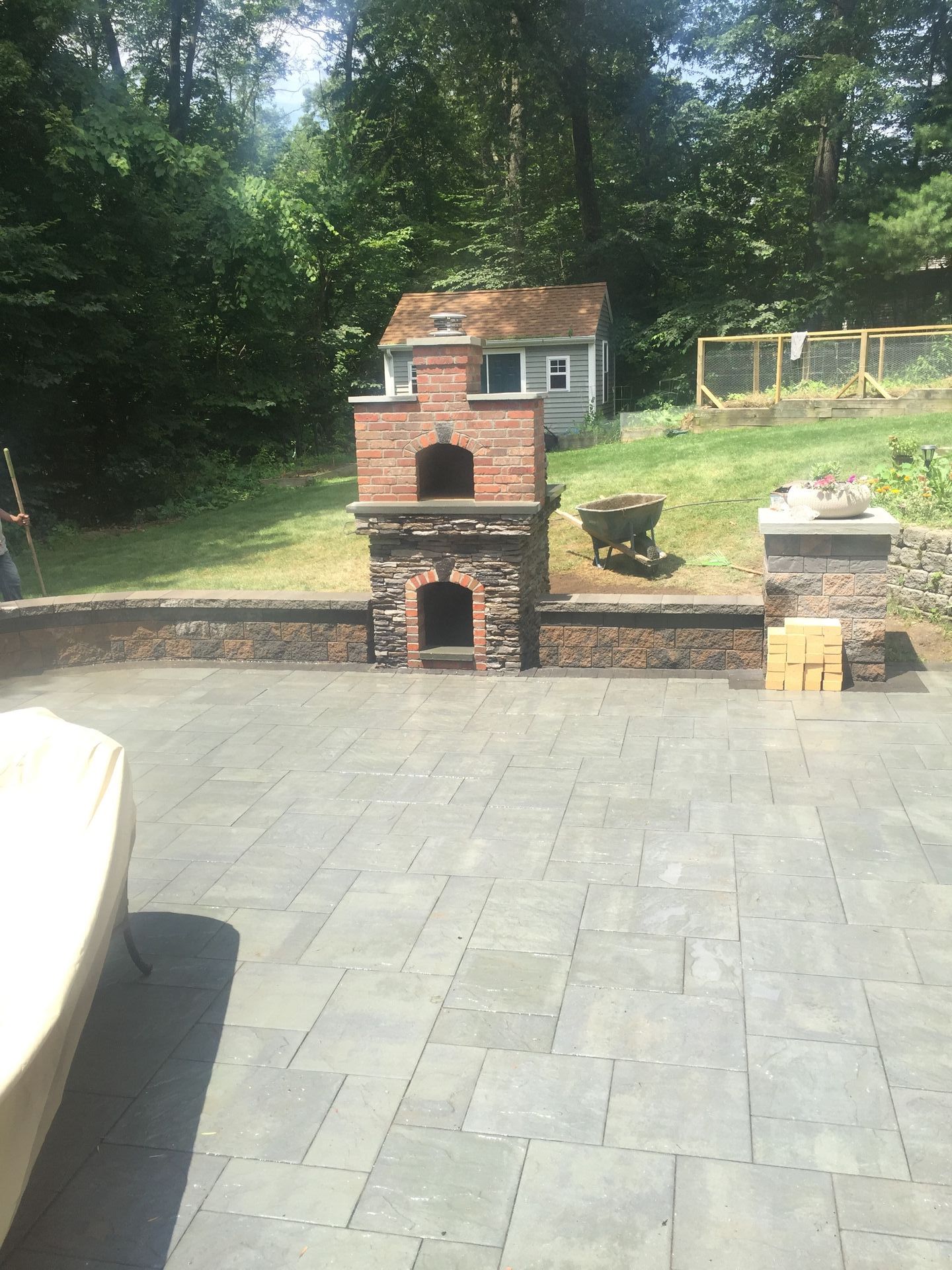 A patio with a brick fireplace and a small house in the background