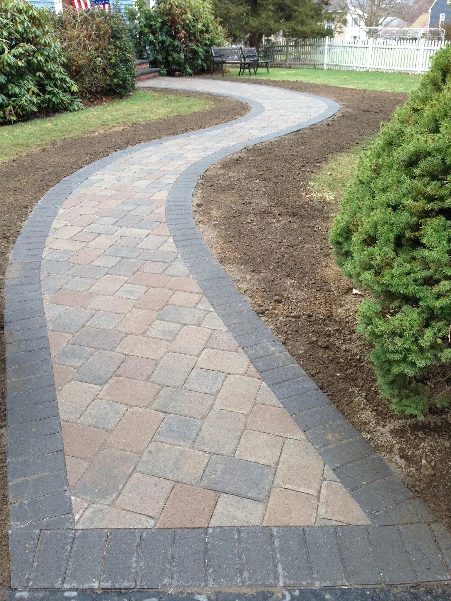 A brick walkway in a park with a bench in the background